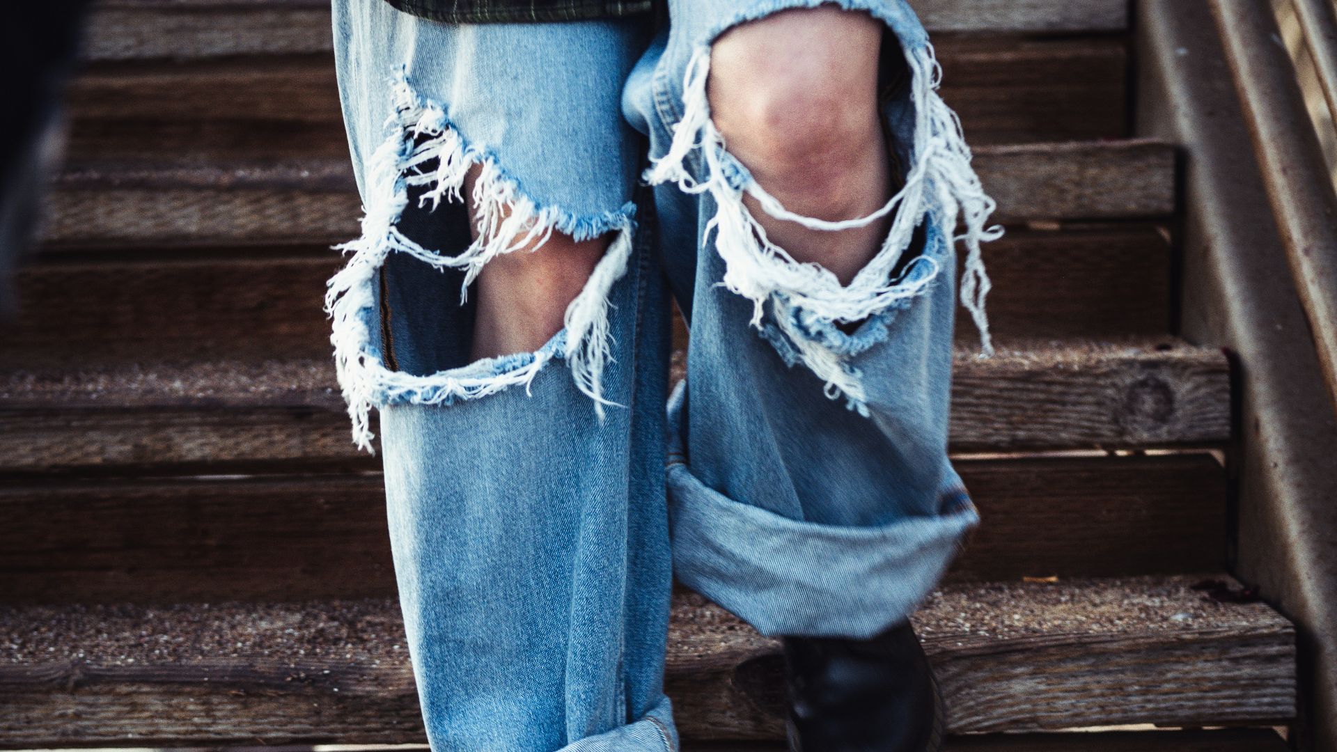 a person's legs in jeans and a blue shirt on a wooden staircase