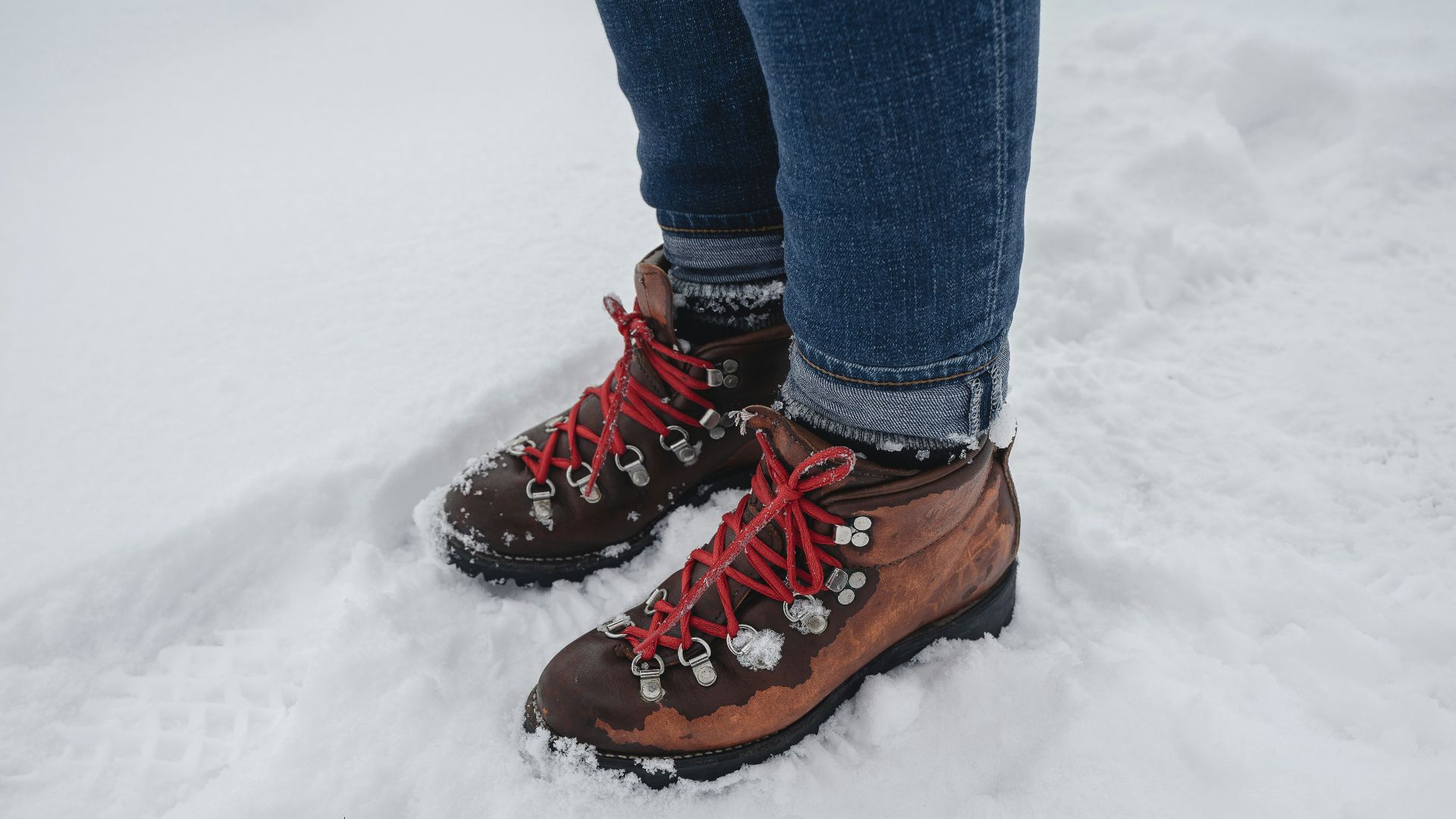 person in blue denim jeans and brown leather boots standing on snow covered ground during daytime