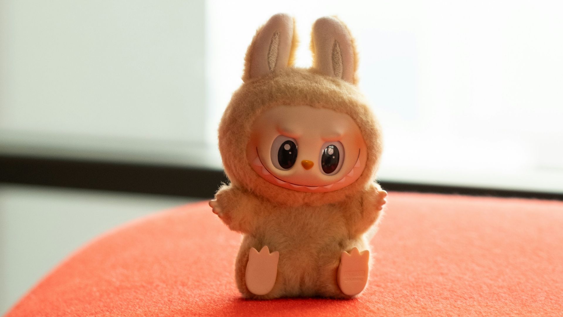 A cute toy is sitting on a red cushion.