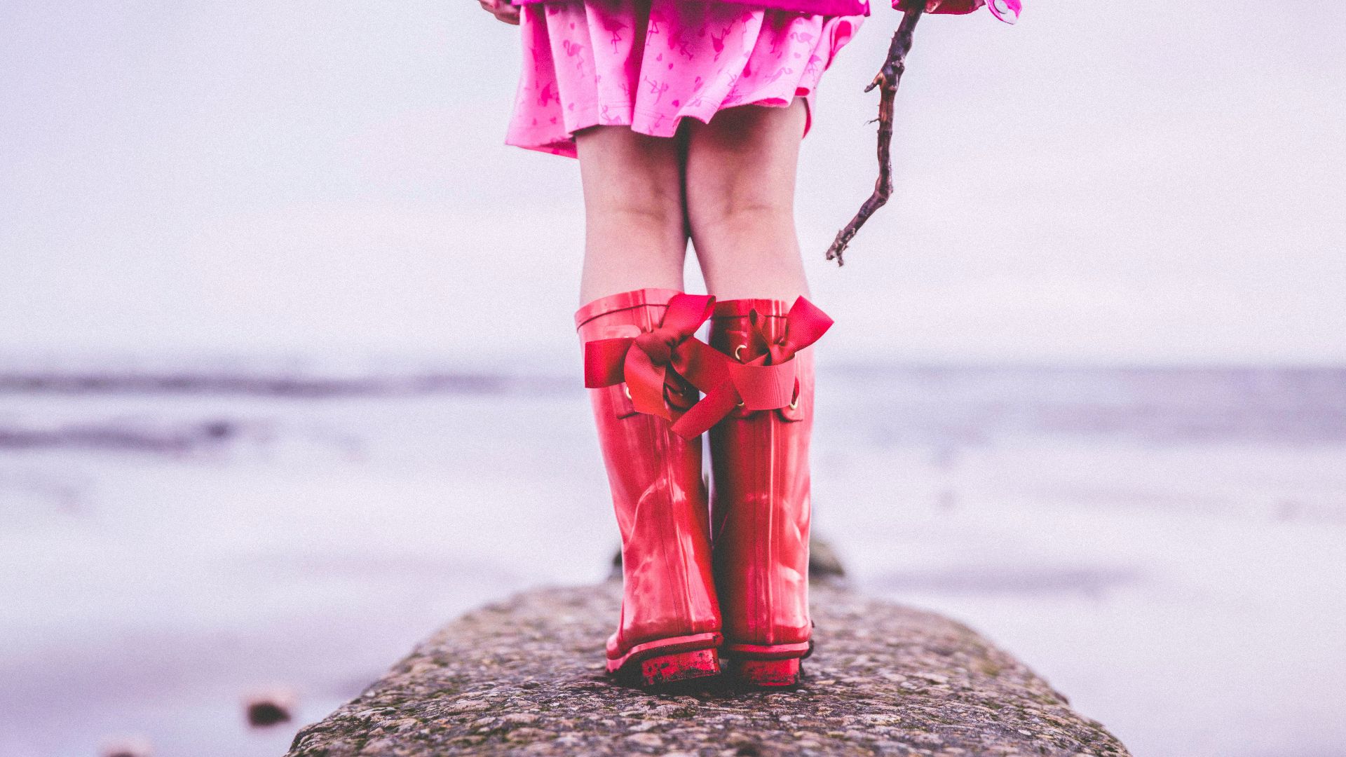 woman in pink dress and red boots standing on beach shore during daytime