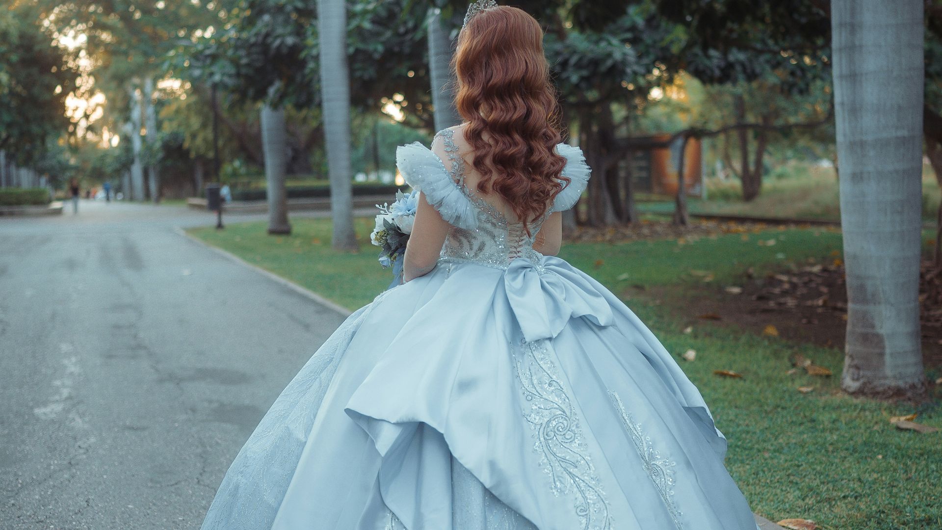 Woman in a light blue ballgown walking in a park.