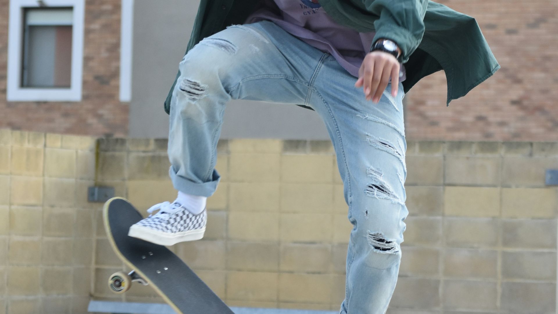 man in green hoodie and blue denim jeans sitting on skateboard during daytime