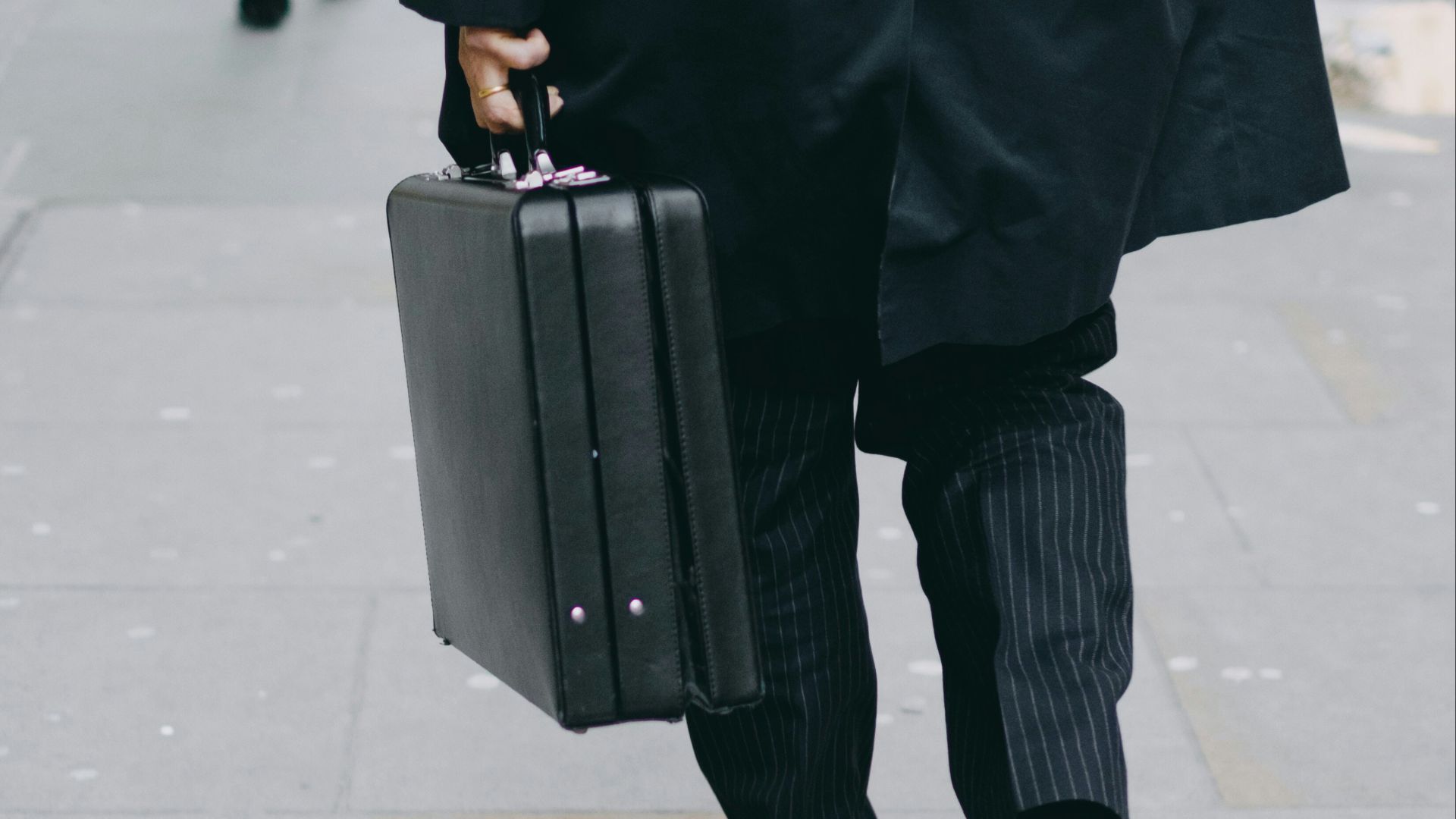 person carrying suit case while walking on pavement