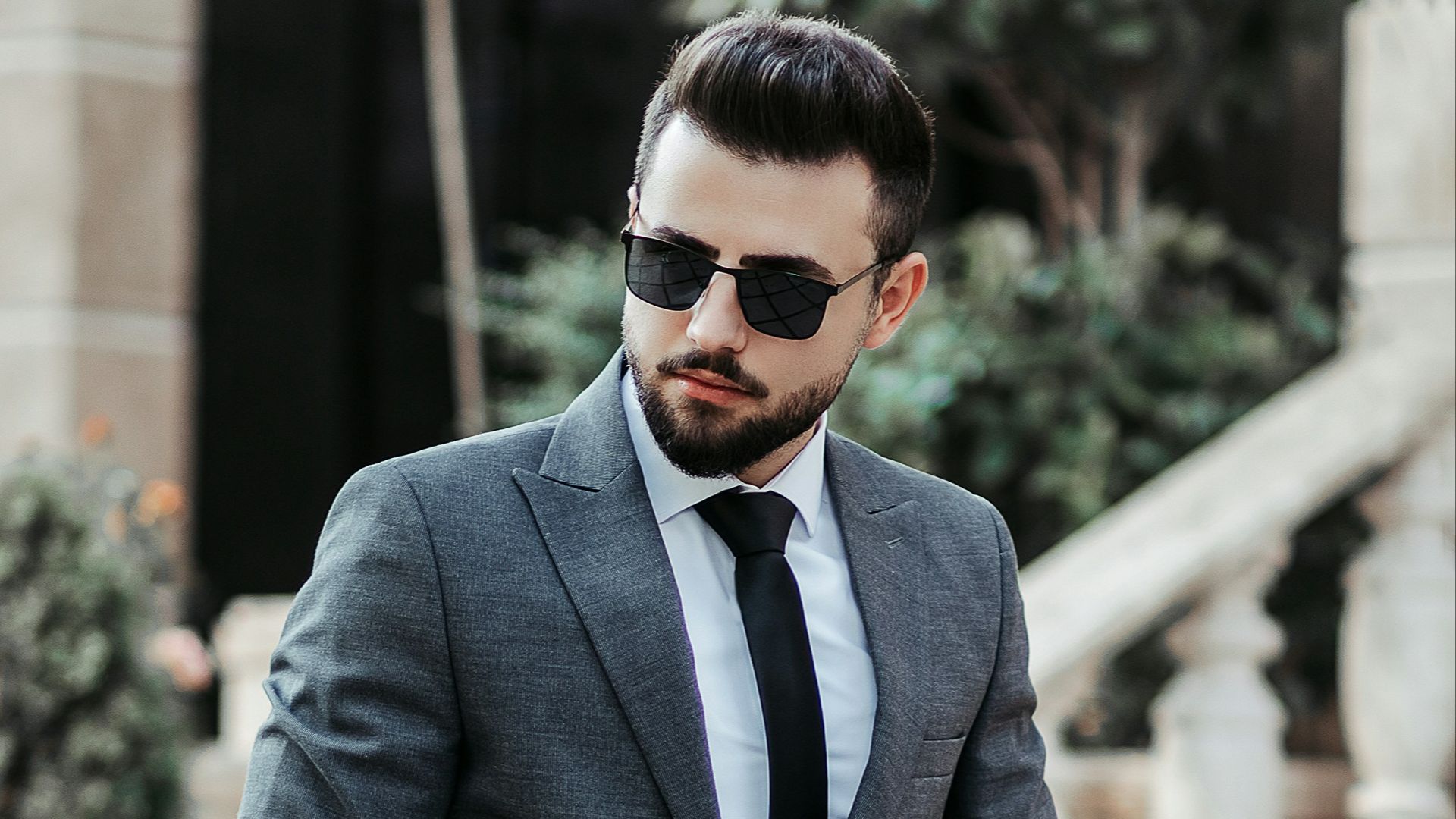 man in gray suit jacket and black pants wearing black sunglasses standing on gray concrete stairs