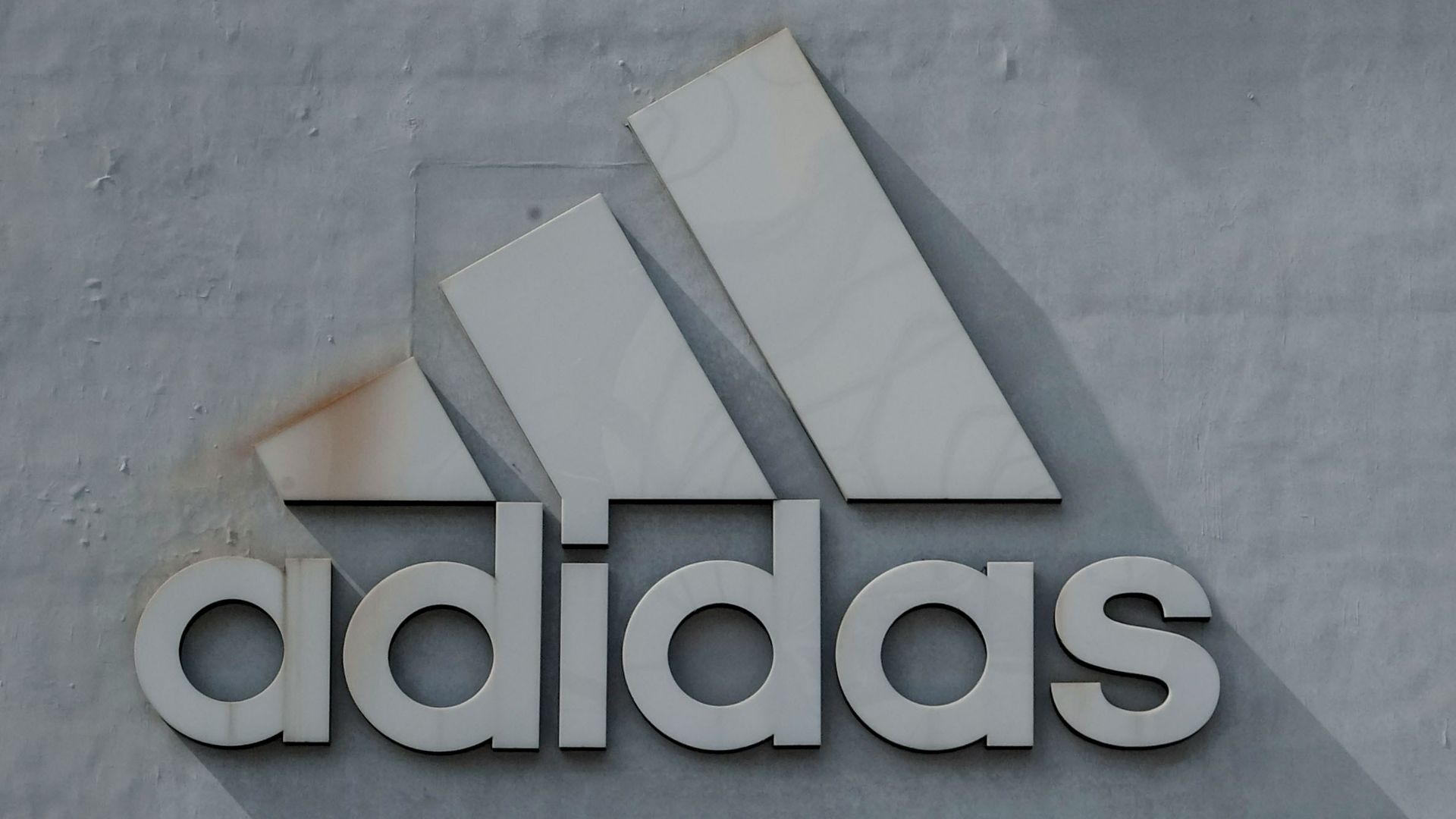 man standing in front of boy leaning on adidas building wall