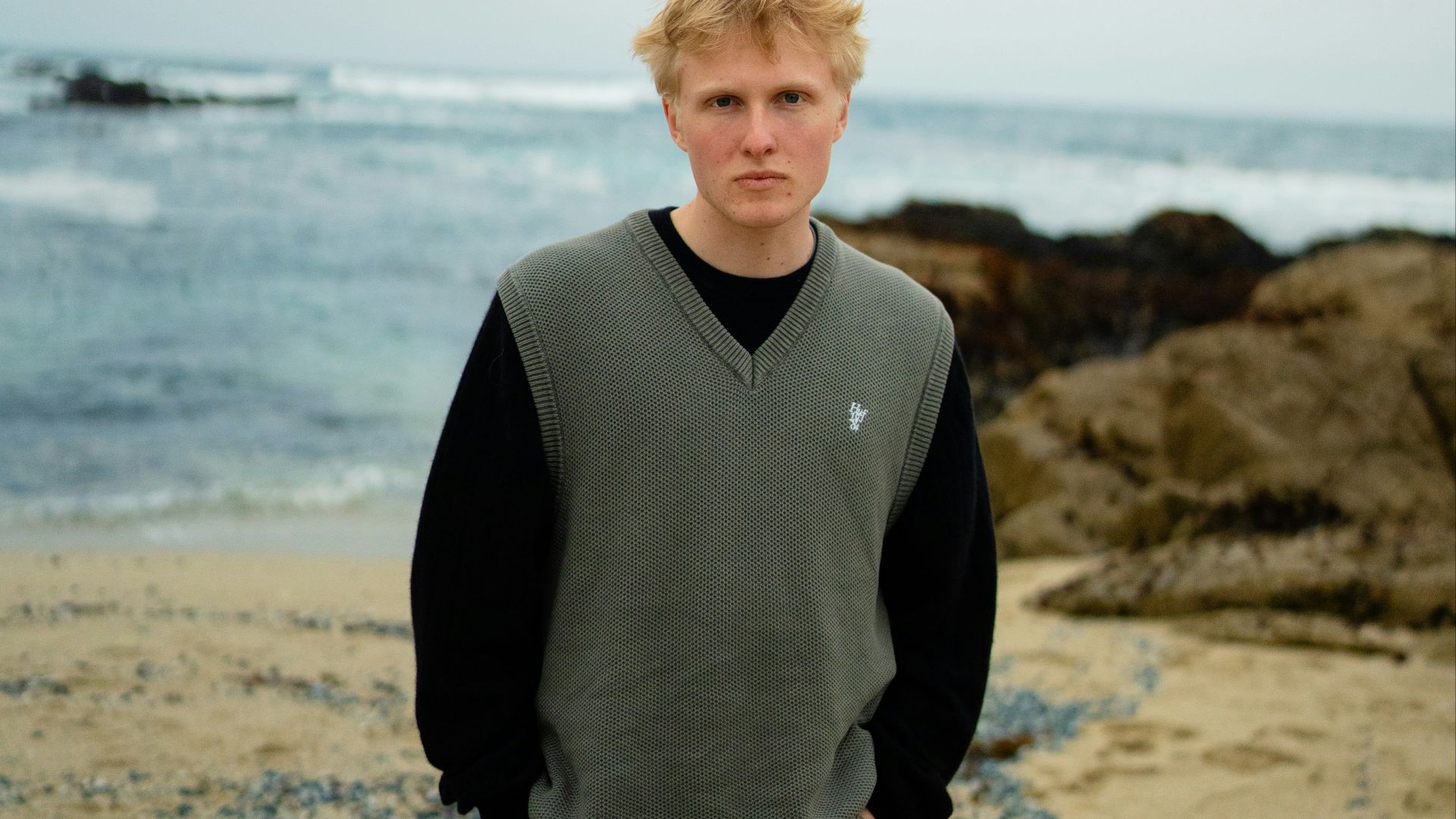 A young man stands on a beach.