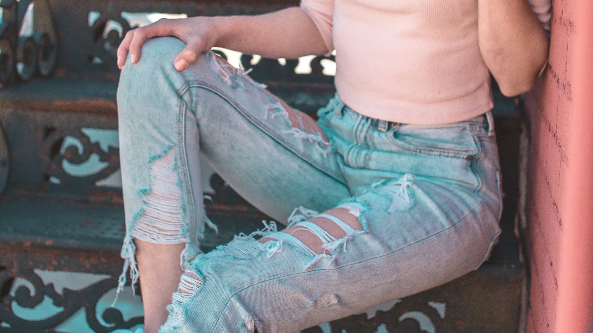woman wearing pink half-sleeved top and distressed acid-washed jeans sitting on staircase