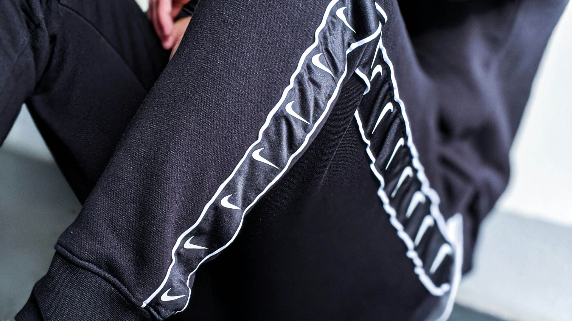 person in black and white pants and white sneakers sitting on gray floor tiles