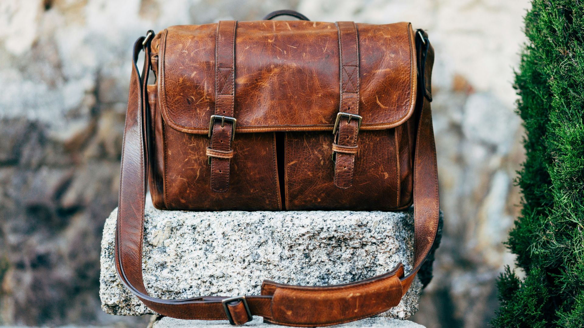 brown leather satchel bag on gray concrete surface near green plant at daytime
