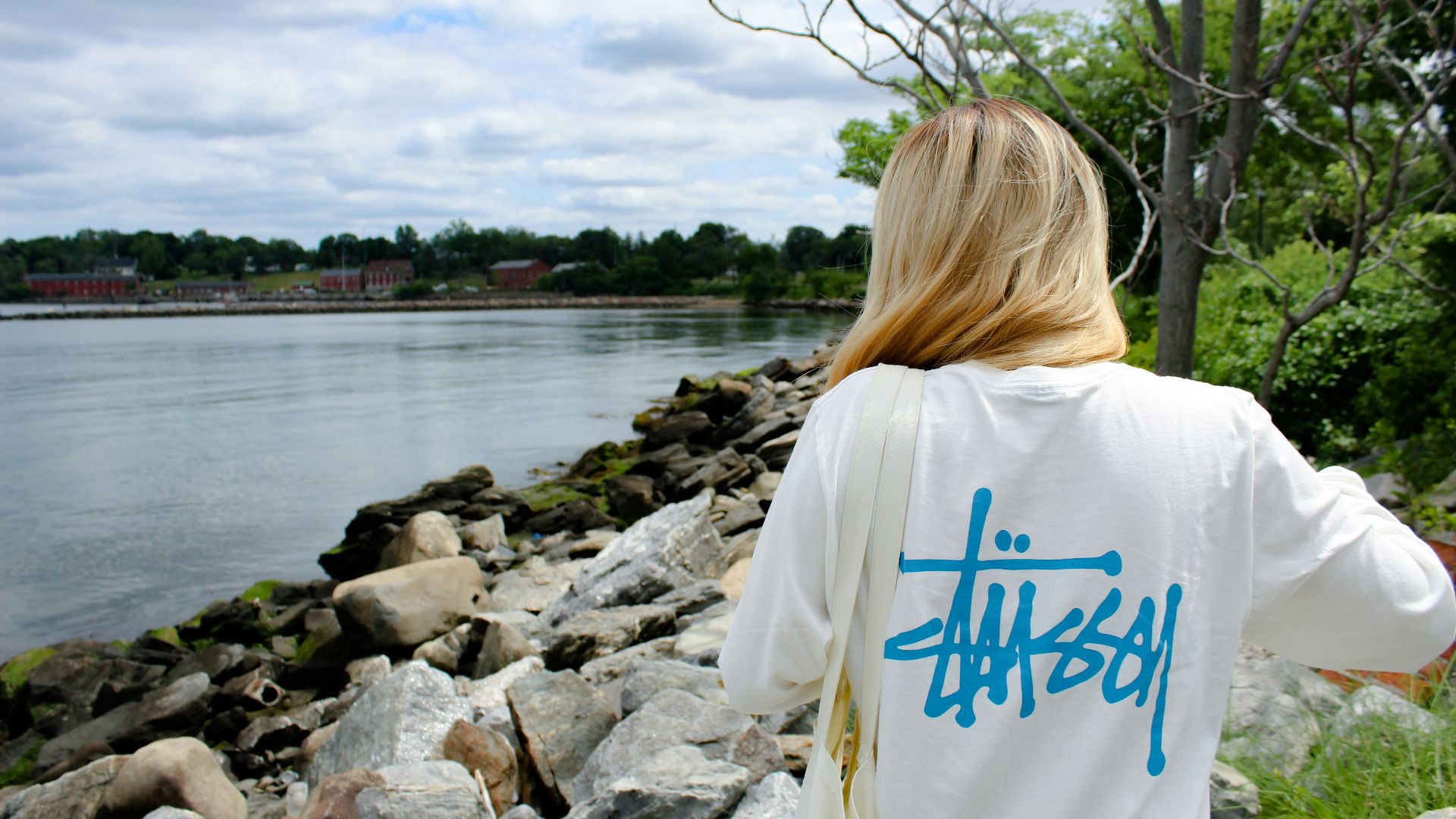 woman in white and blue shirt standing on rocky shore during daytime