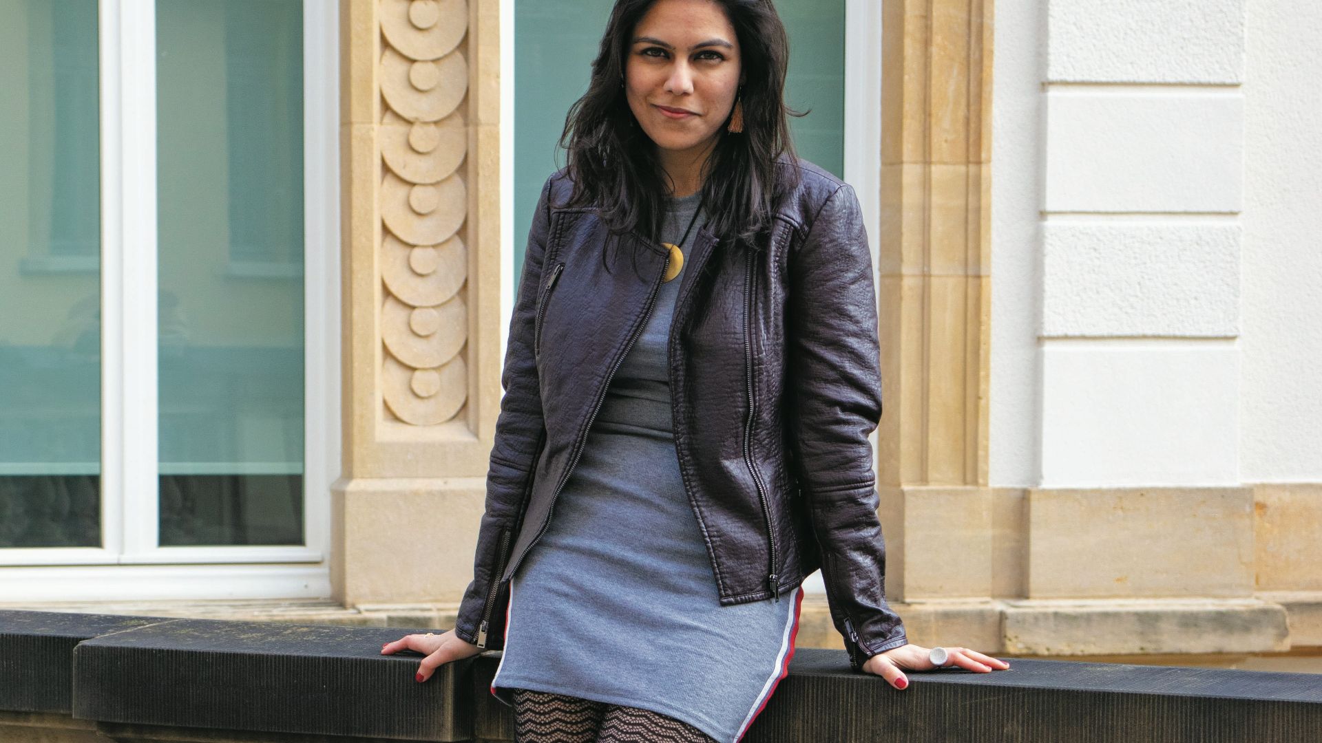 woman in purple coat and black skirt standing on gray concrete stairs