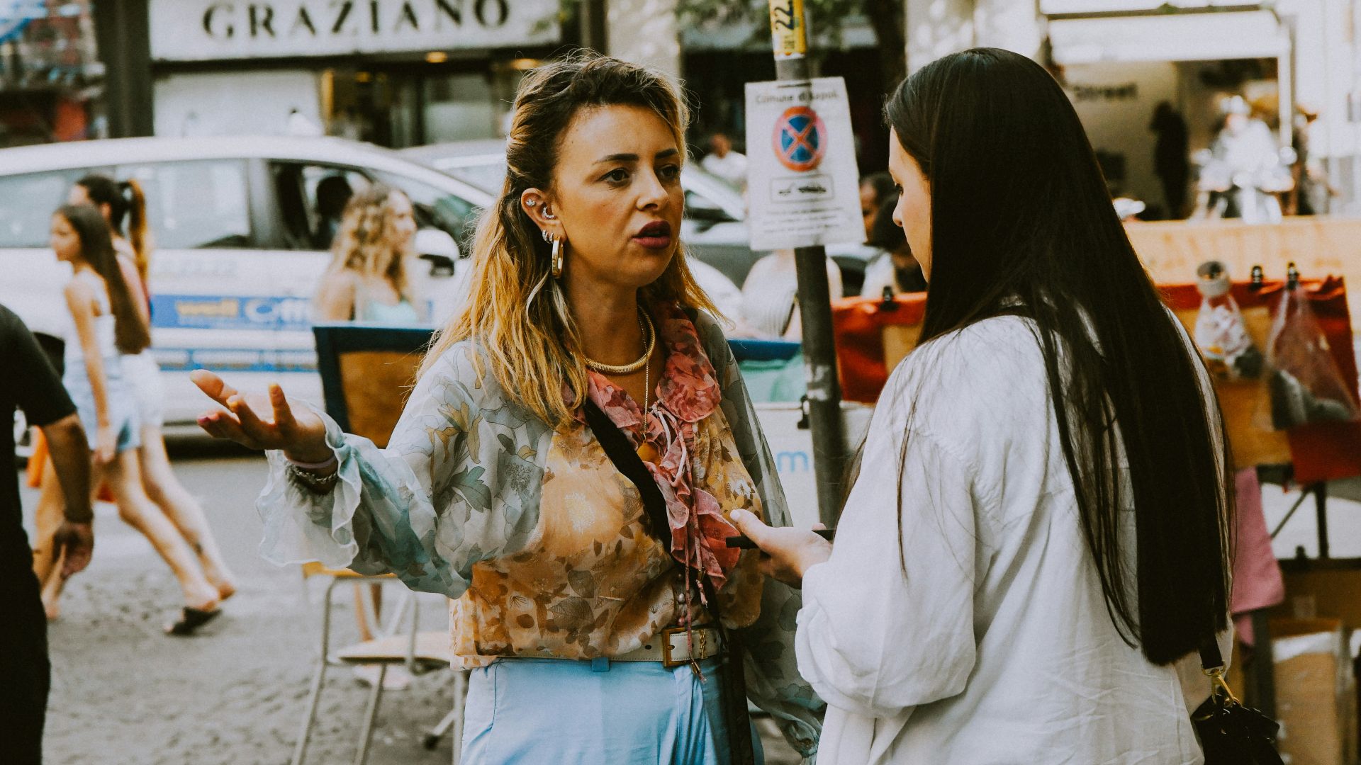 Two women standing on a street corner talking to each other