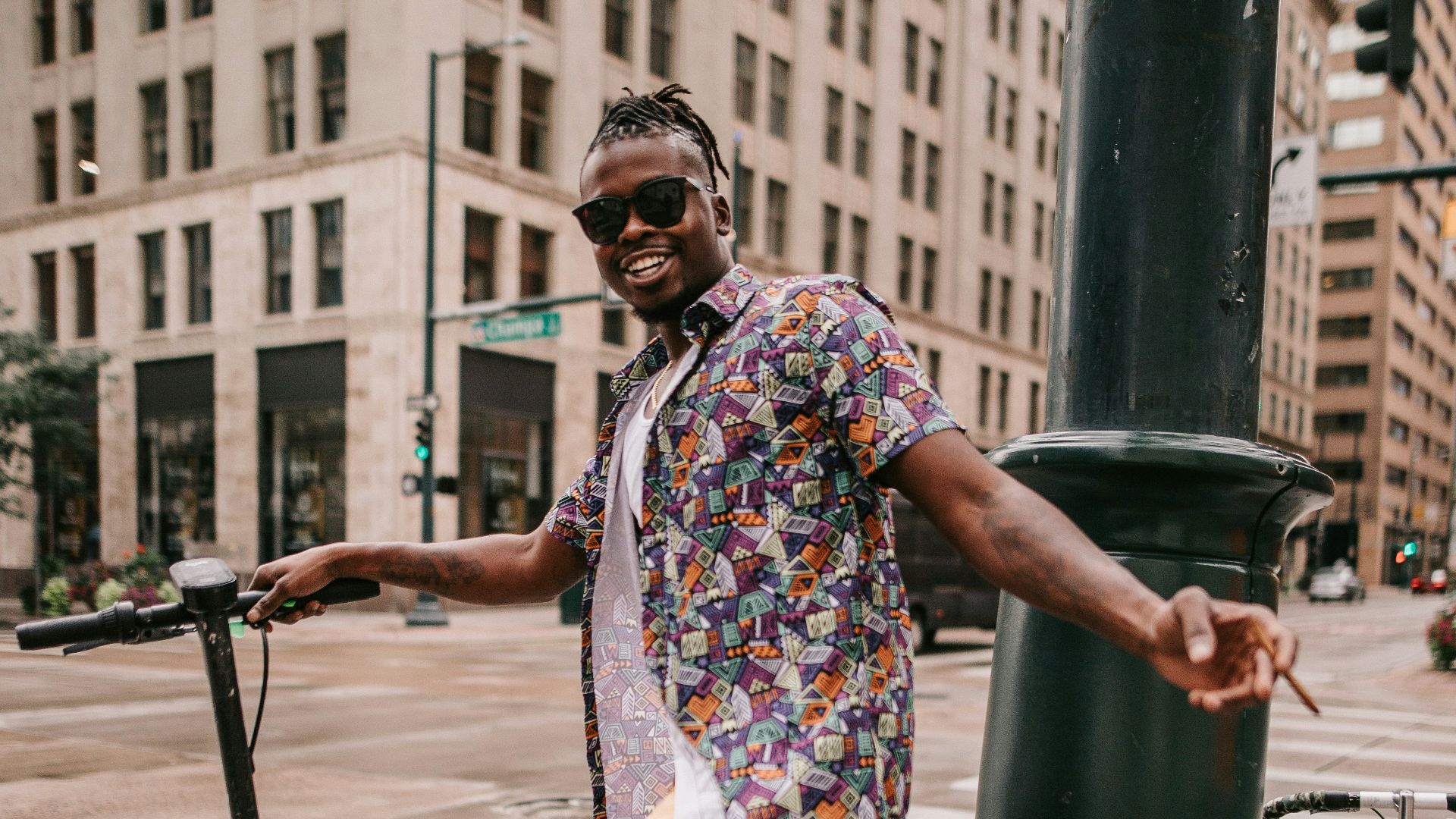 a man wearing sunglasses and a colorful shirt standing next to a green pole