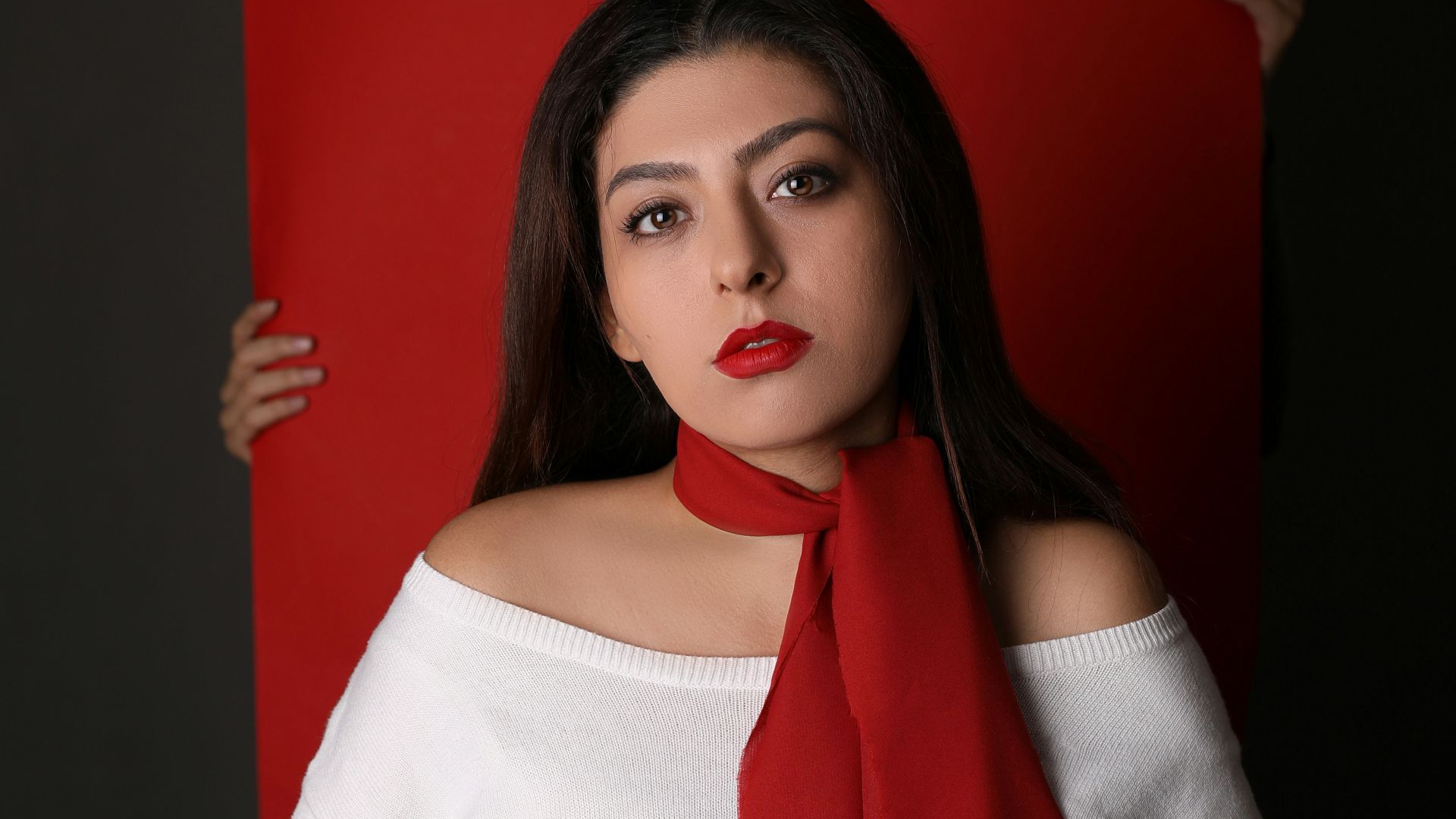 woman in white long-sleeved top and red scarf in front of red paper board