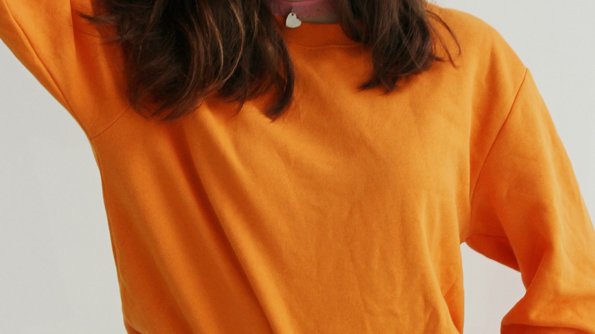 woman wearing orange crew-neck sweatshirt standing while putting right hand on her head