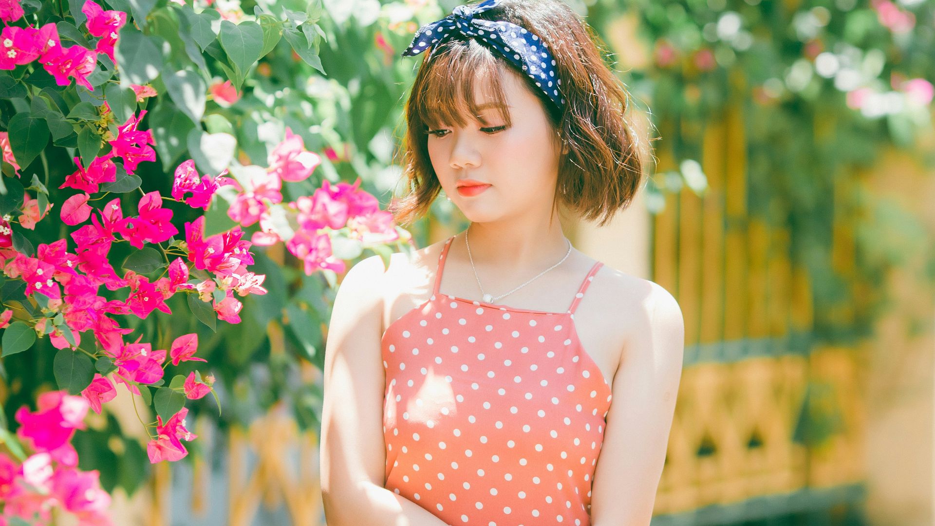 woman in orange polka-dot spaghetti strap dress standing near pink and green plants