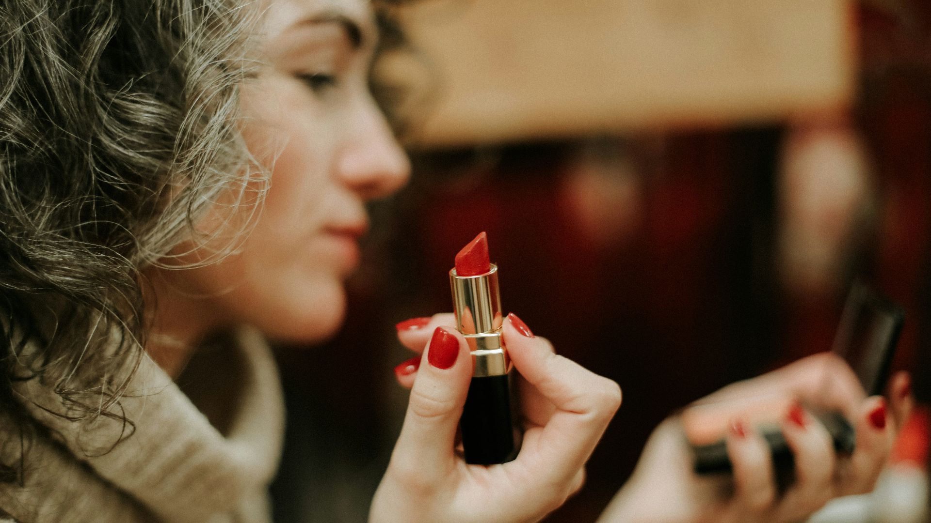 woman in gray sweater holding lipstick