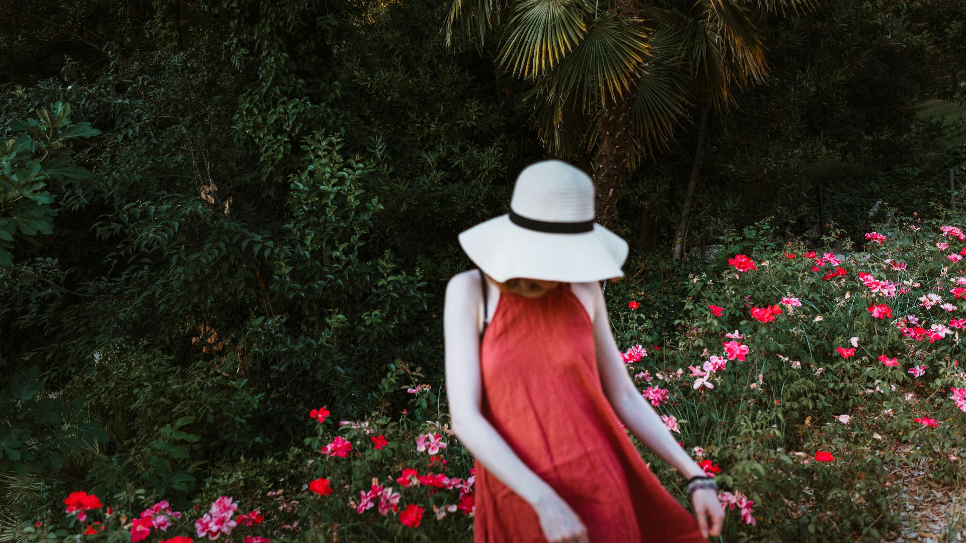 woman in red dress wearing white hat standing in front of green plants