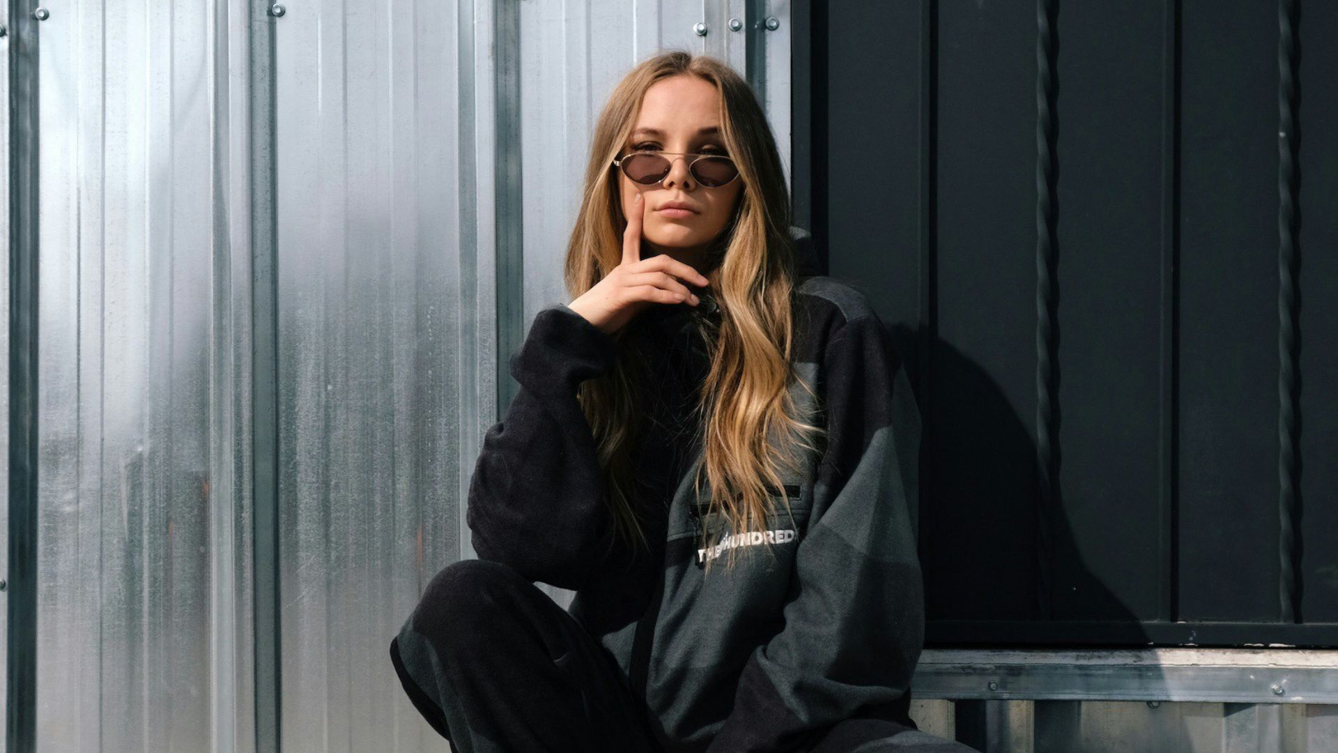 woman in black jacket and white pants sitting on gray concrete floor