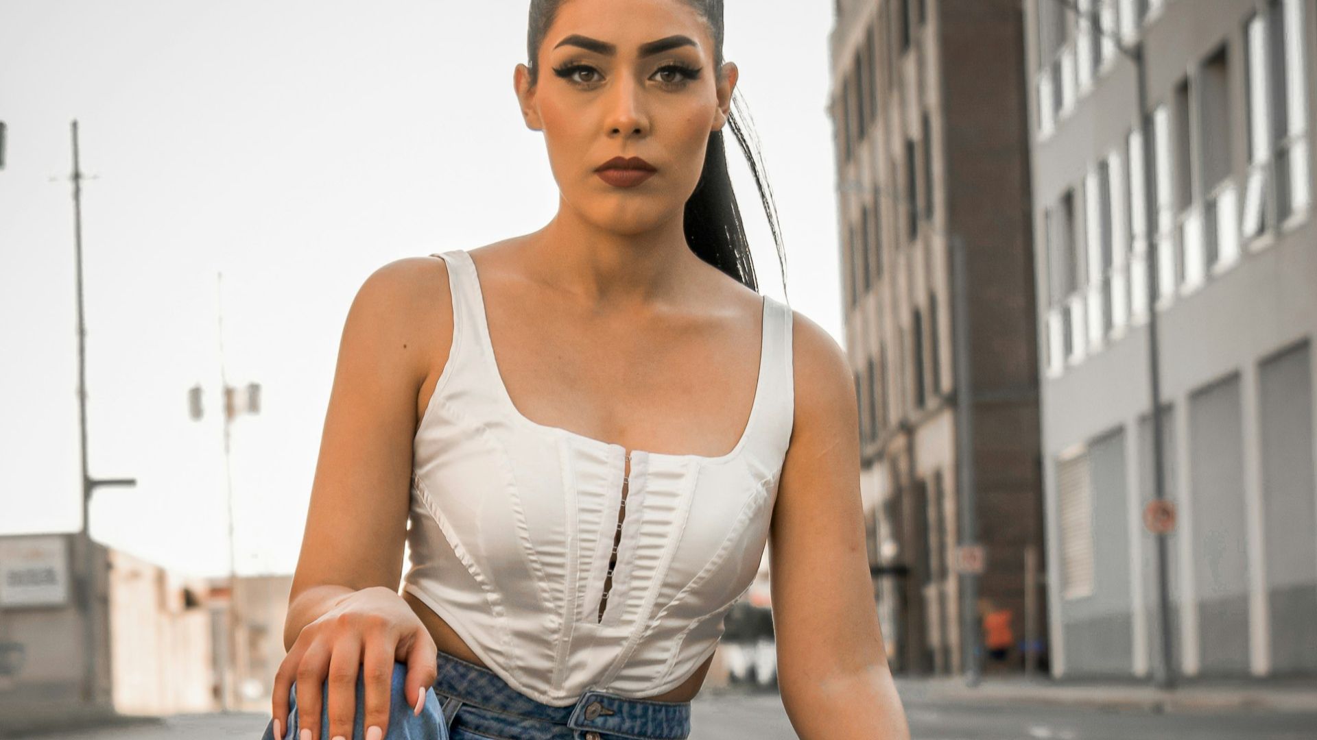 woman in white tank top and blue denim jeans sitting on gray concrete road during daytime