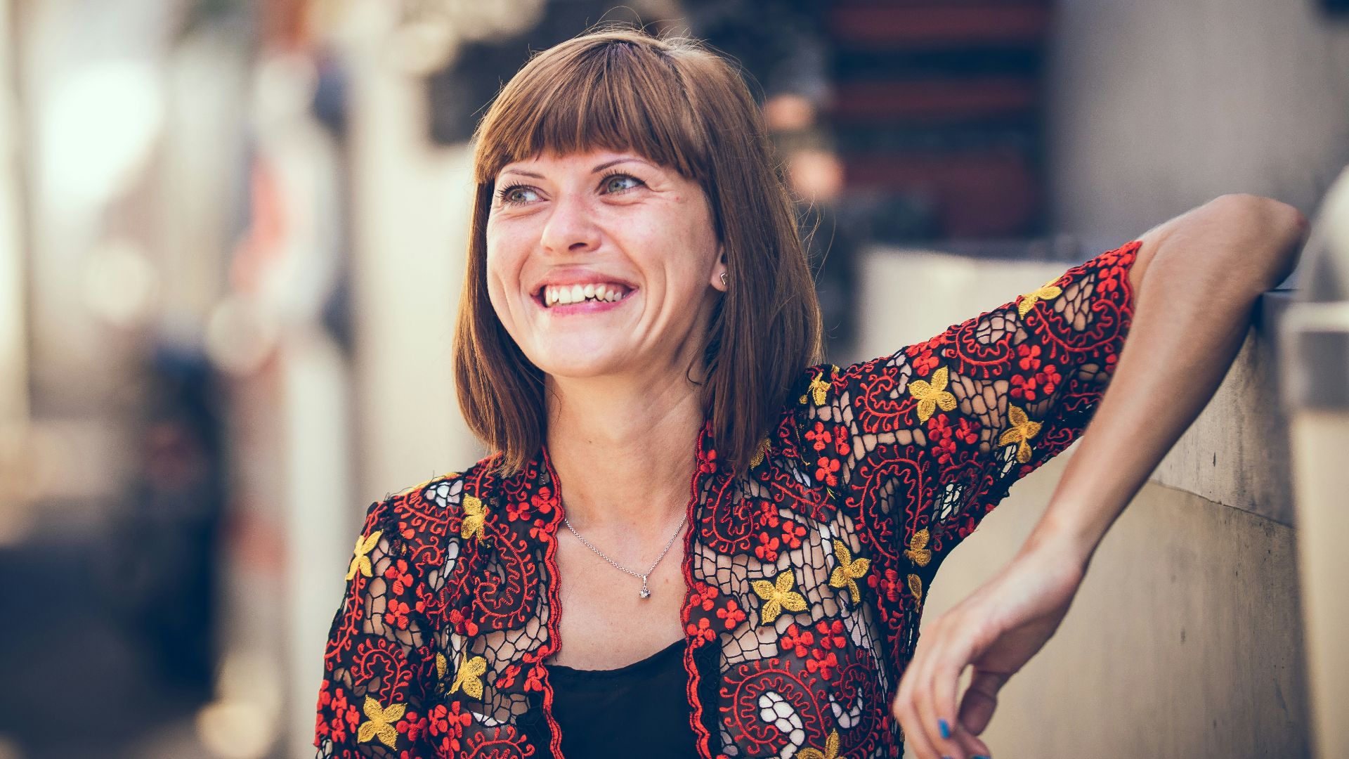woman in floral-themed cardigan leaning on fence in bokeh photography