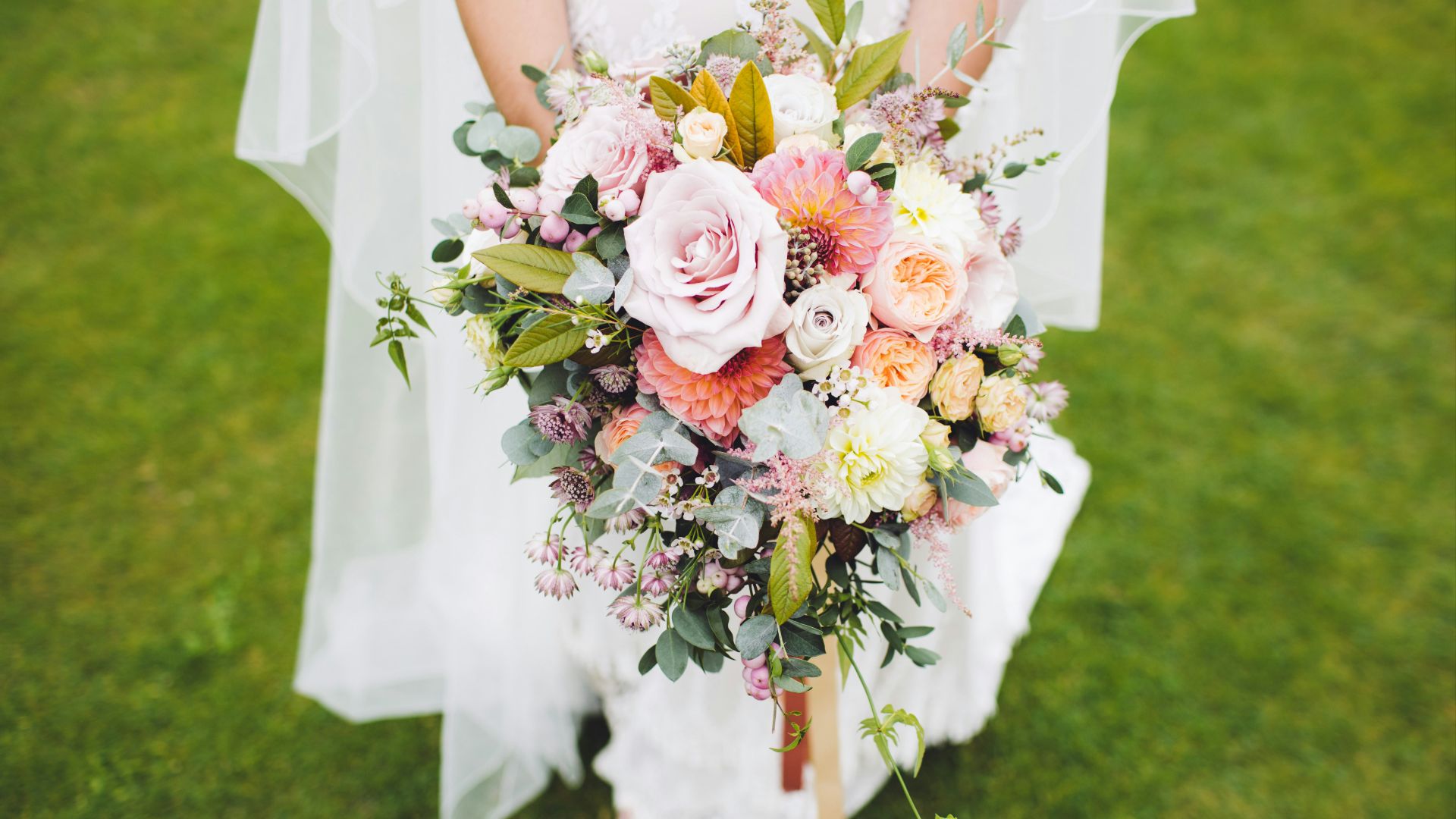 newlywed woman holding bouquet standing on green grass