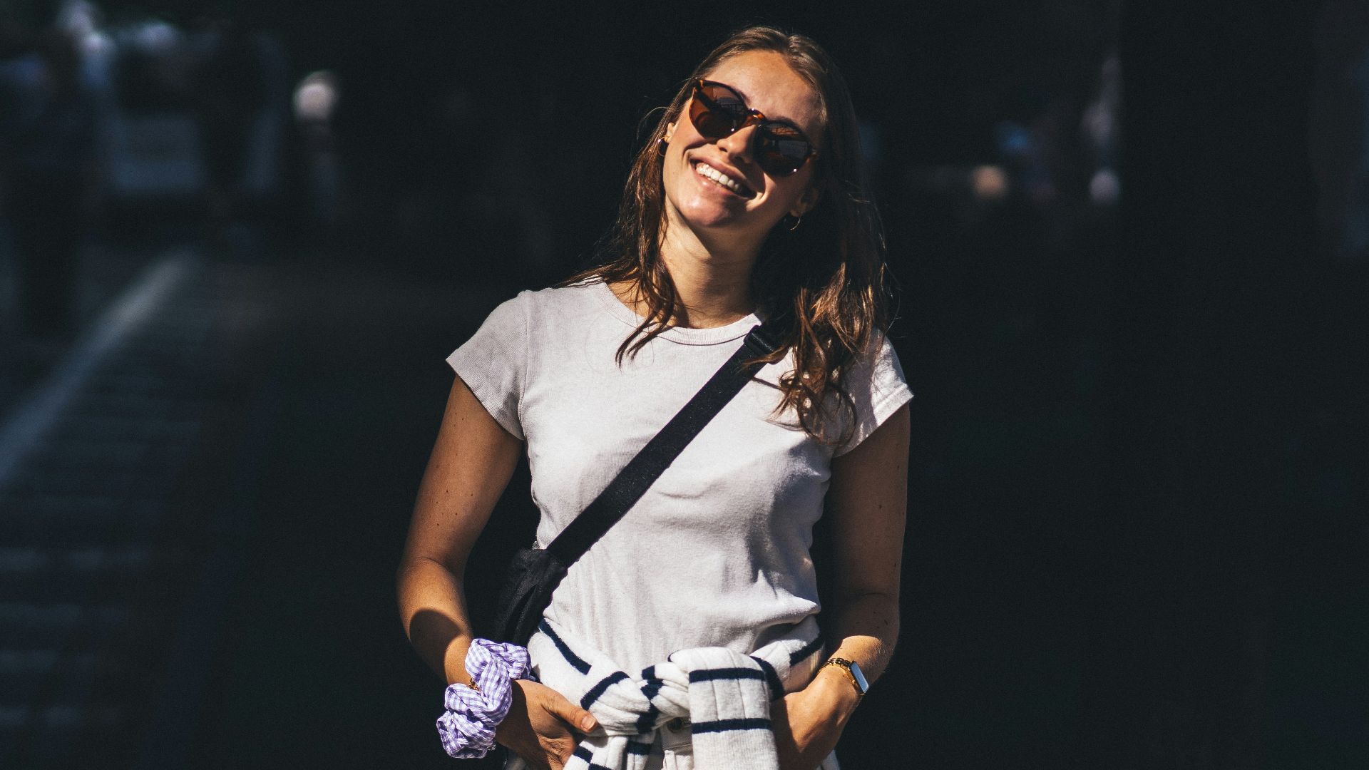 a woman in a white shirt and sunglasses smiles at the camera