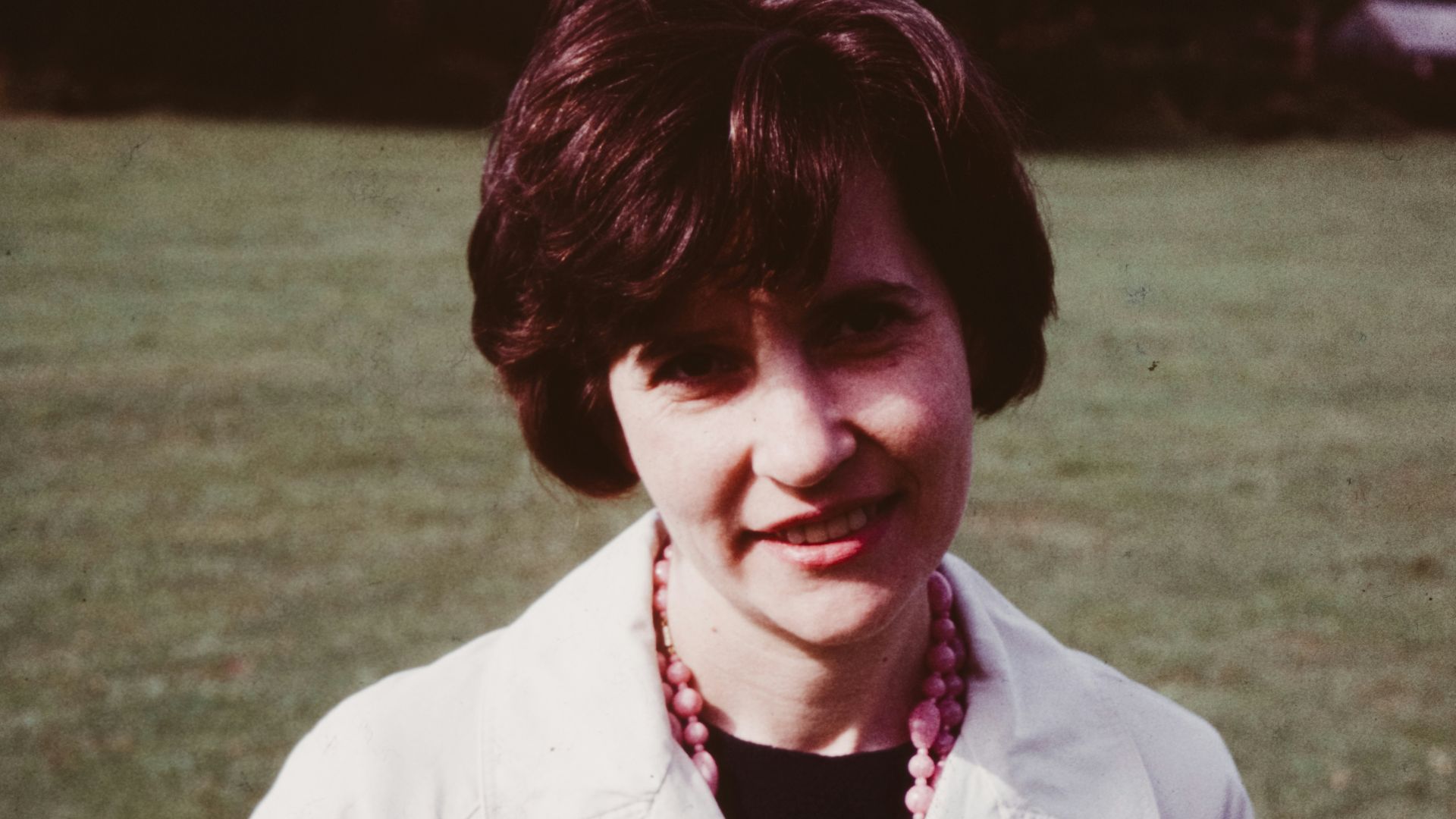 a woman in a white coat standing in a field
