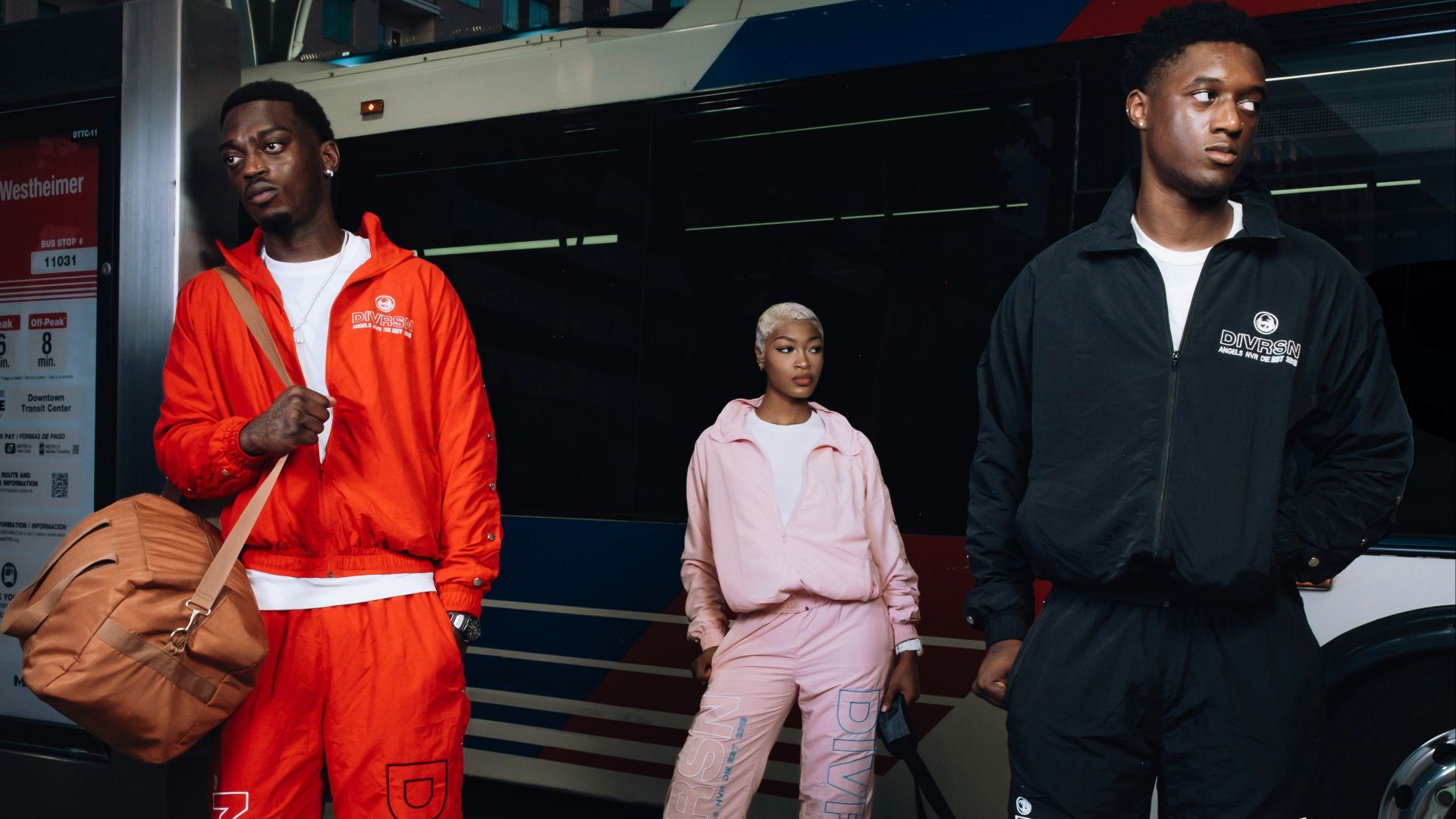 Three people in tracksuits stand near a bus.