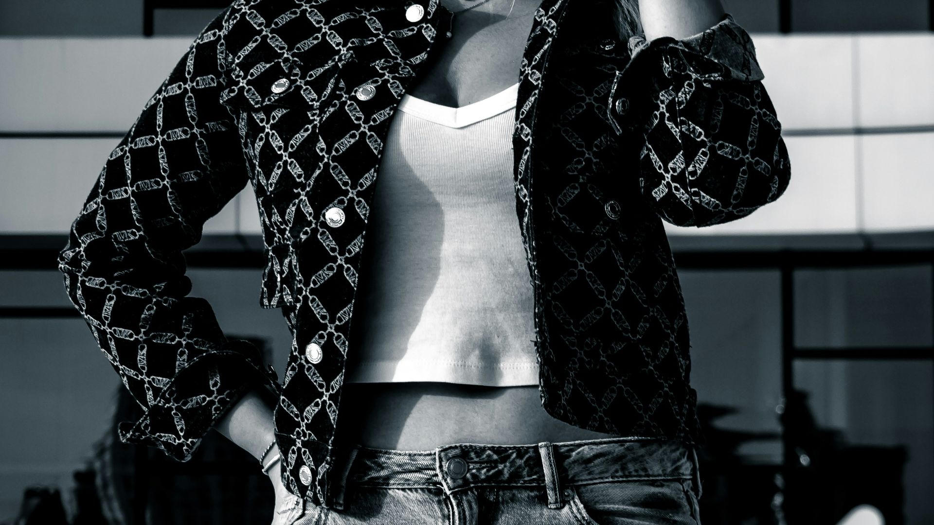 Woman in sunglasses and patterned jacket poses outdoors.