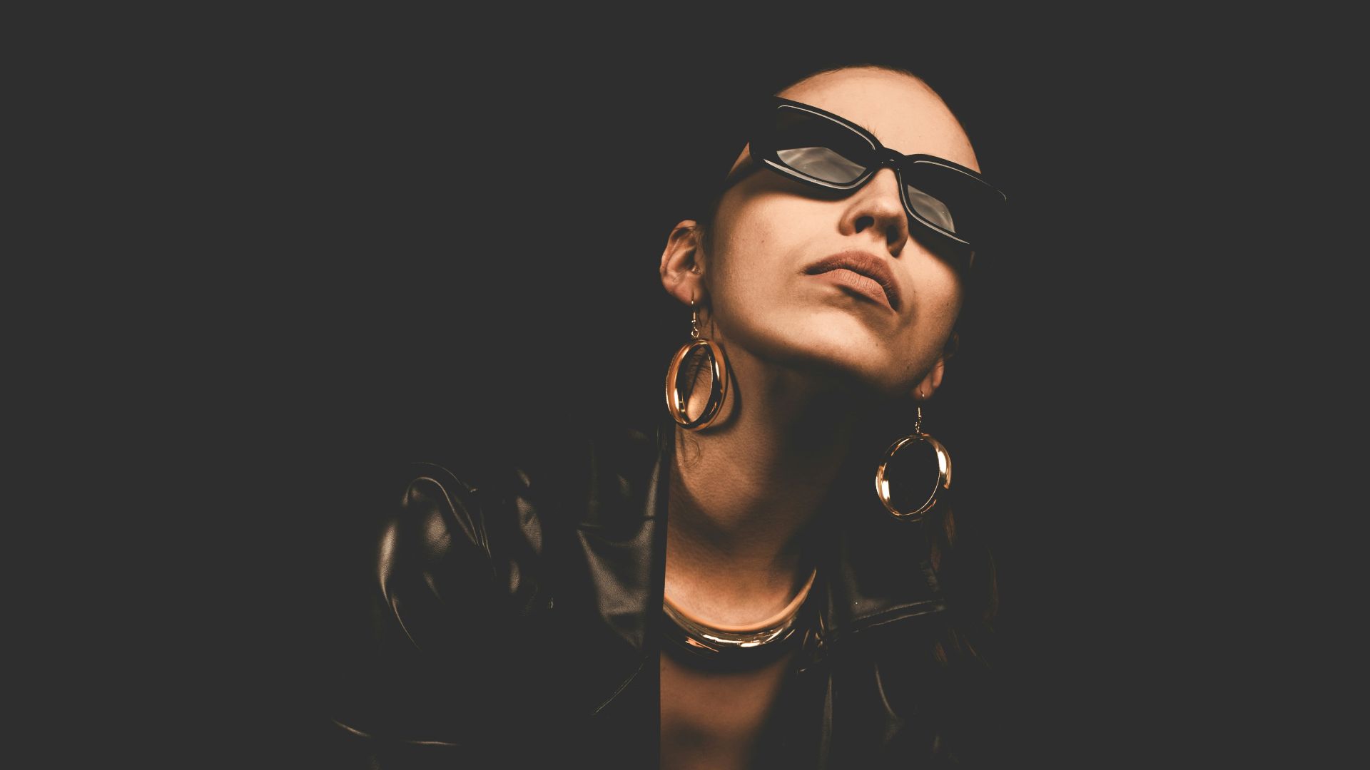 Woman in sunglasses and leather jacket poses dramatically.
