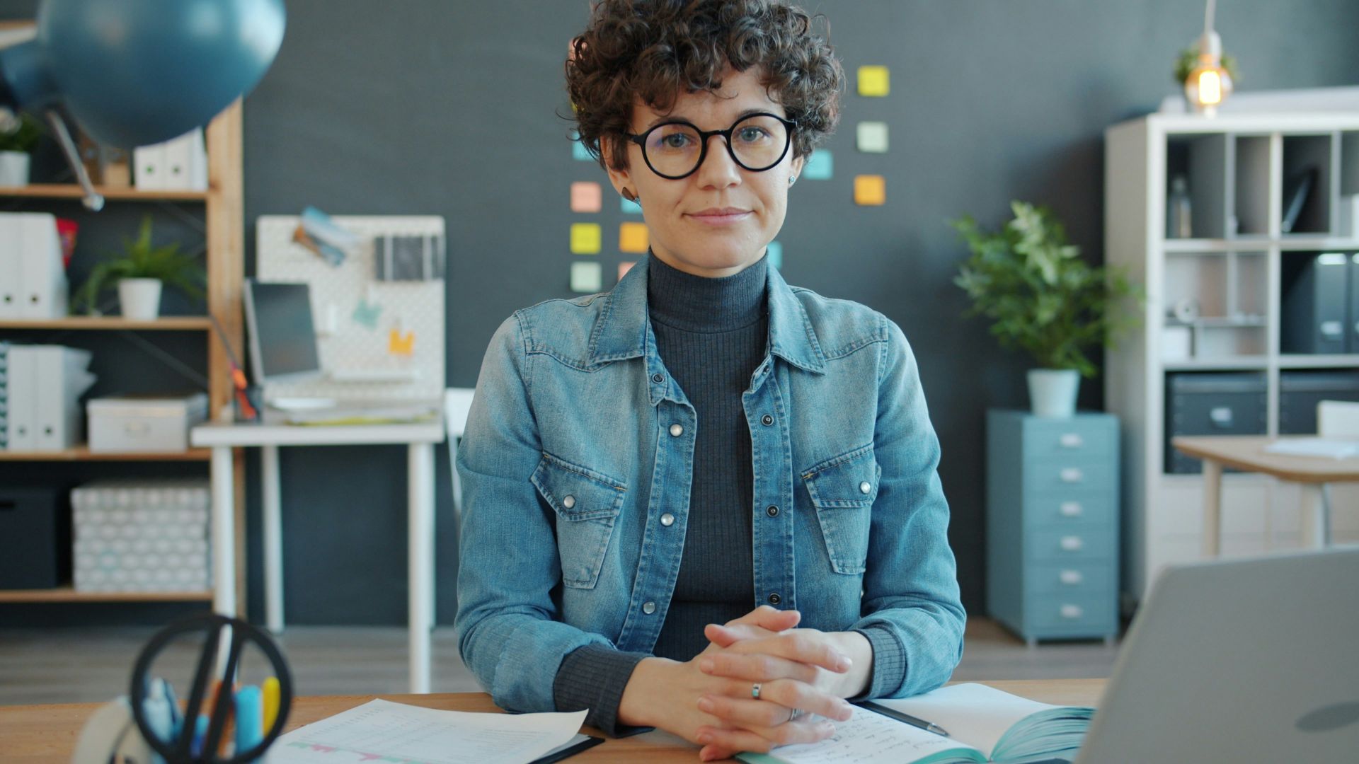A woman with curly hair and glasses in an office.