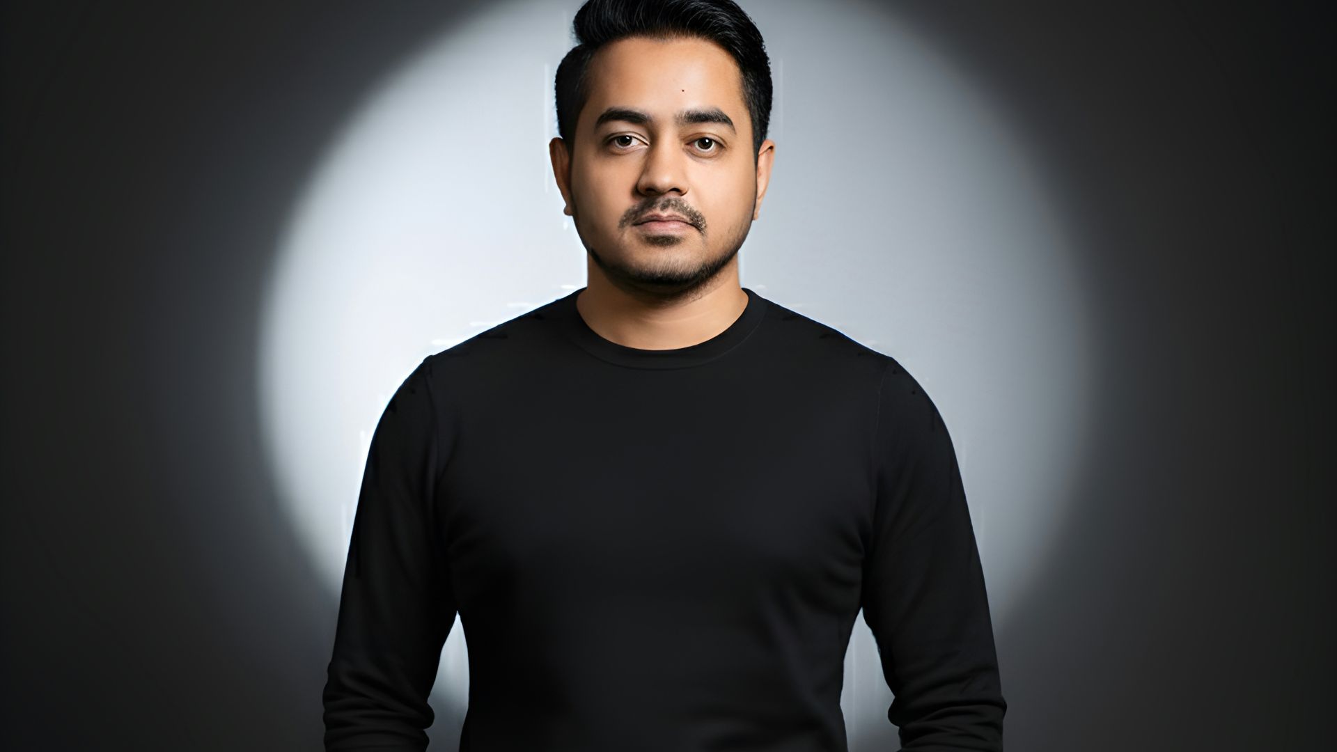 Man in black sweater and pants standing against spotlight.