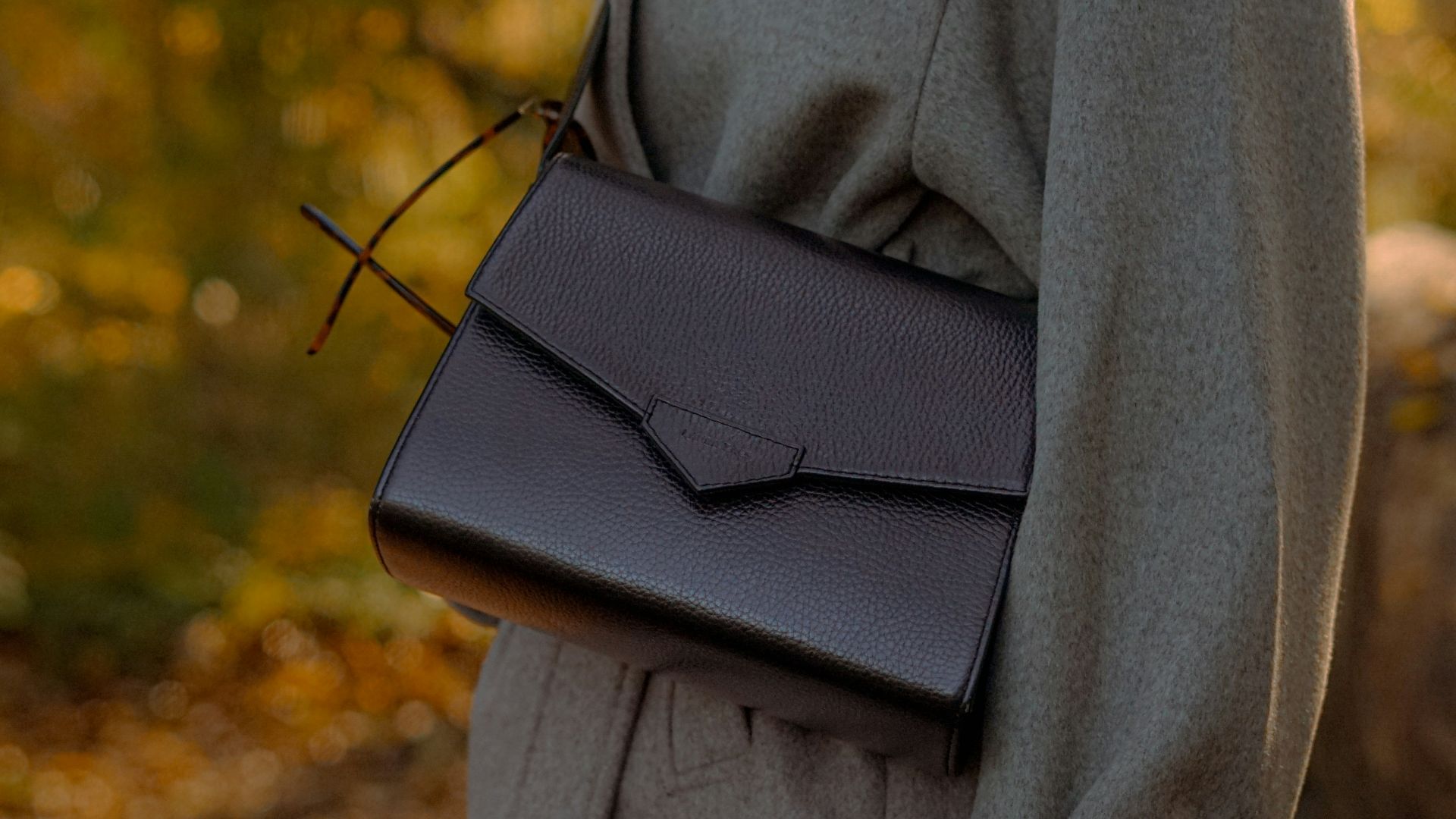 A person holds a stylish black leather handbag.