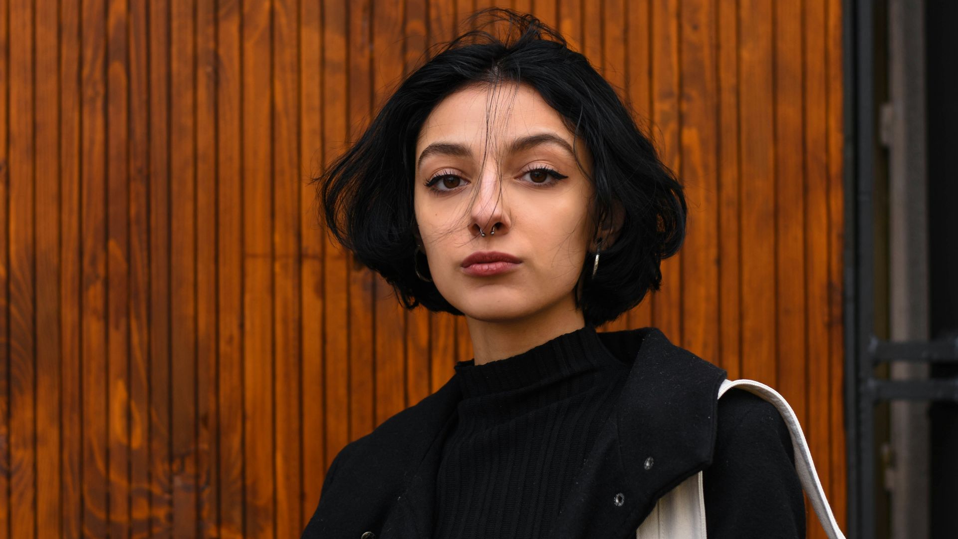 woman in black blazer standing near brown wooden wall