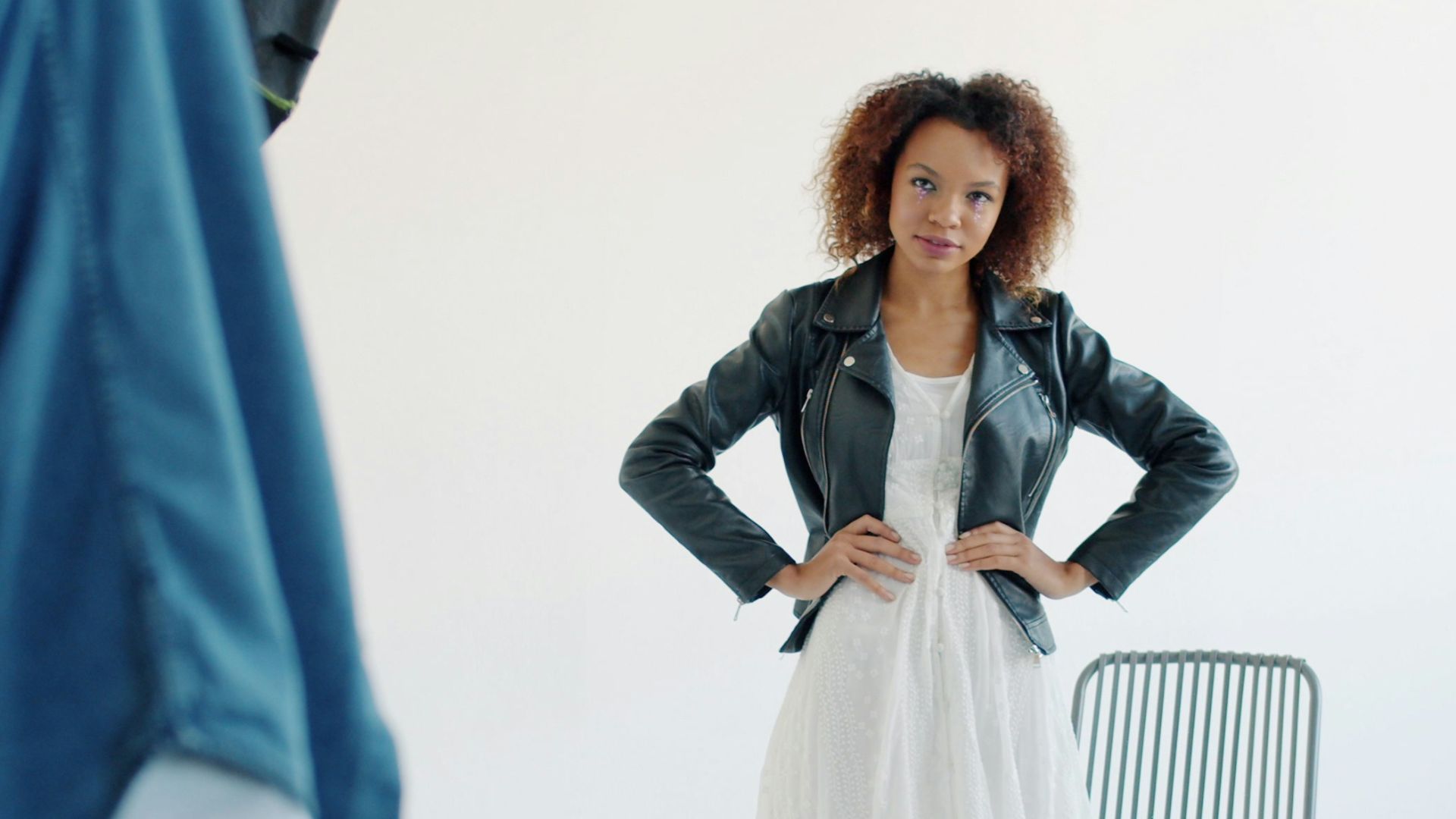 Model posing in a white dress and leather jacket.