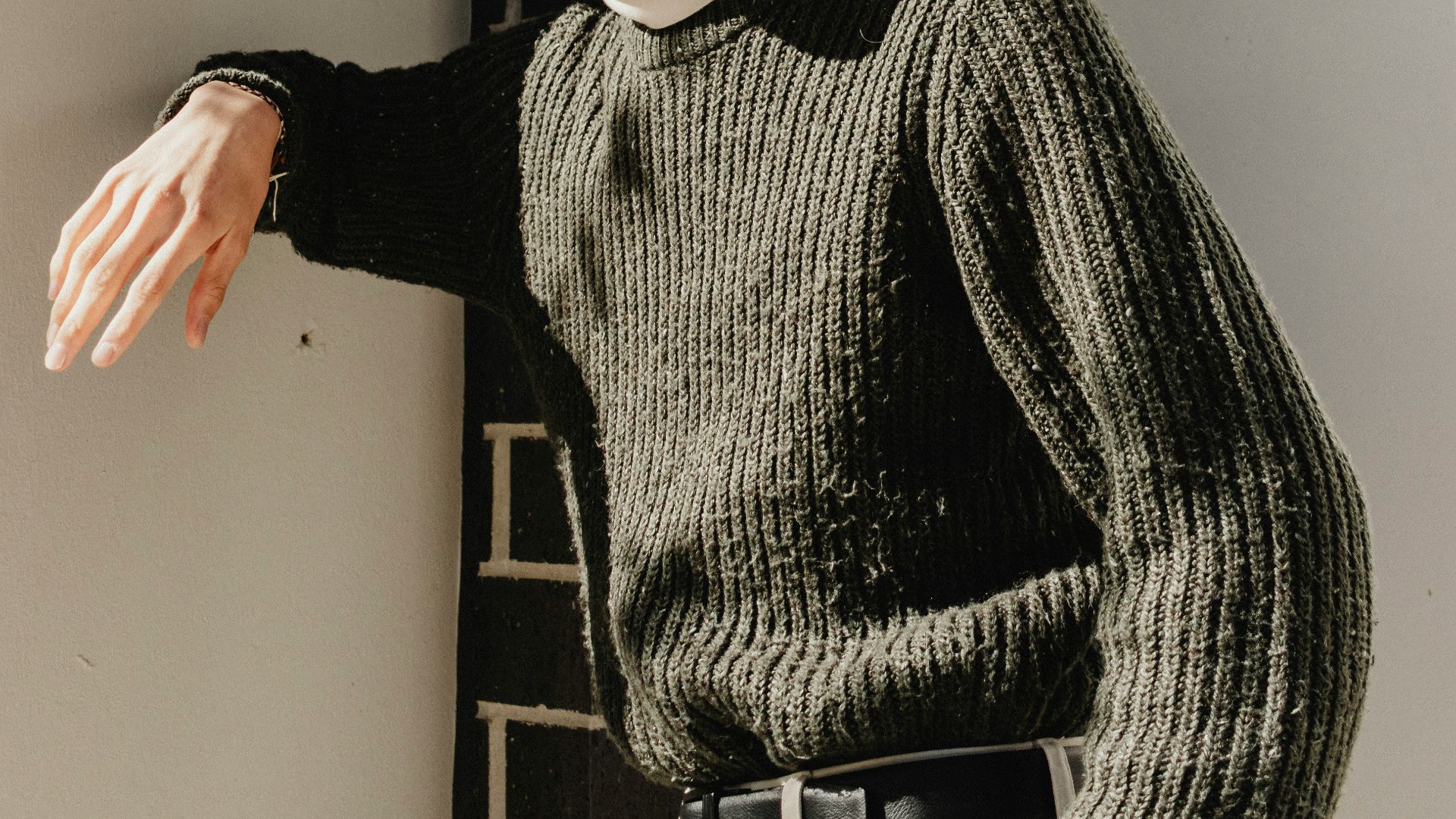 a man wearing glasses leaning against a wall