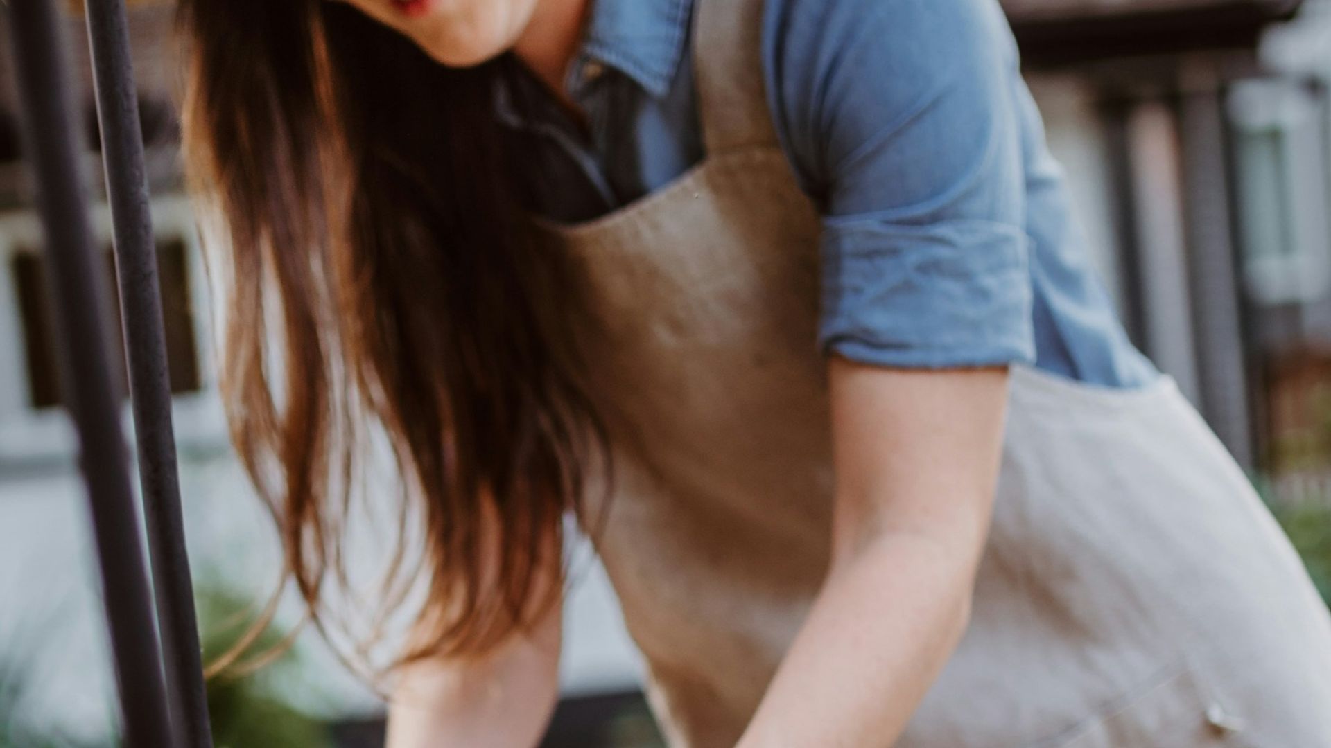 A woman in an apron and hat tending to flowers