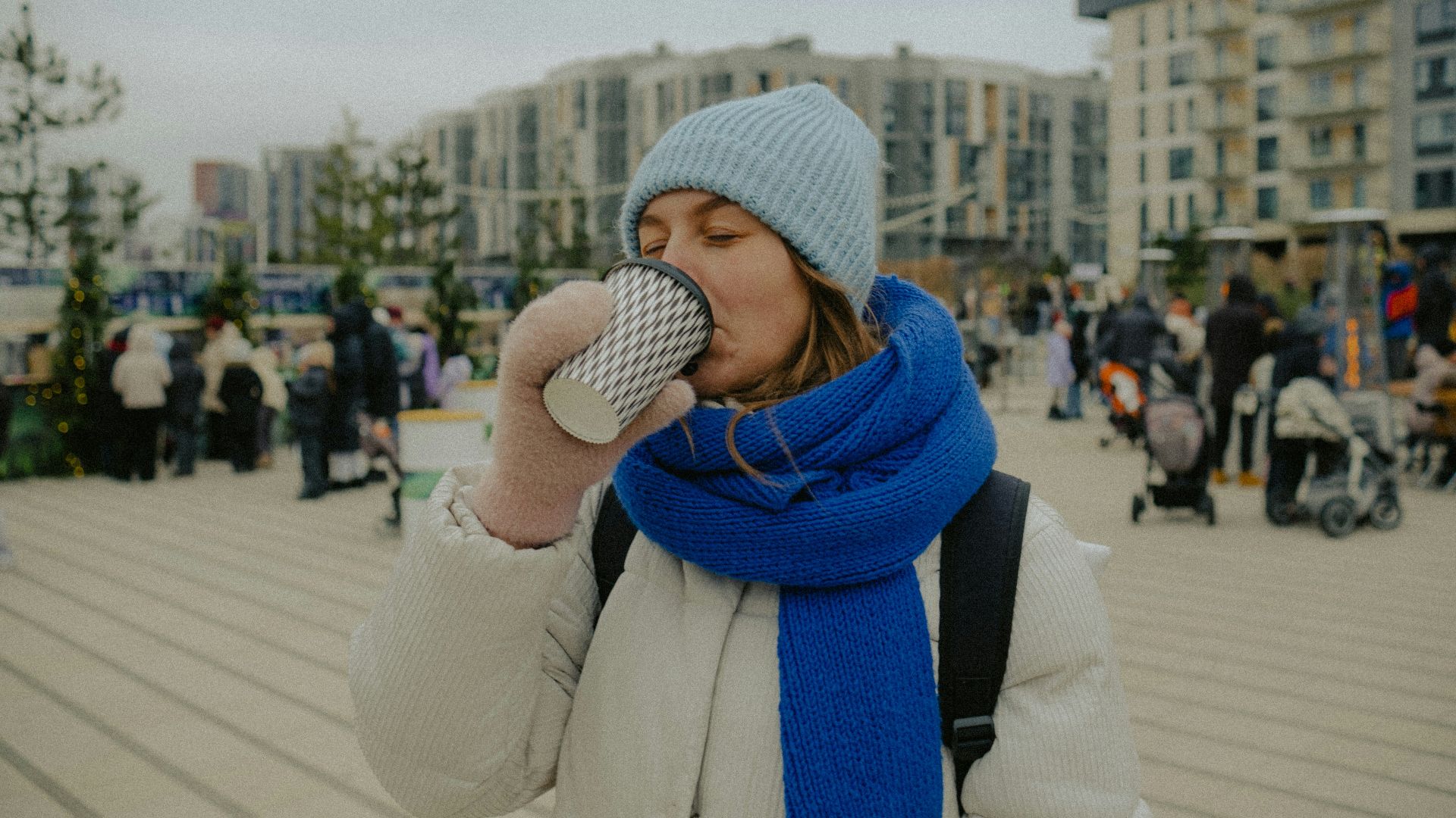 Woman in winter clothes drinks from a cup.