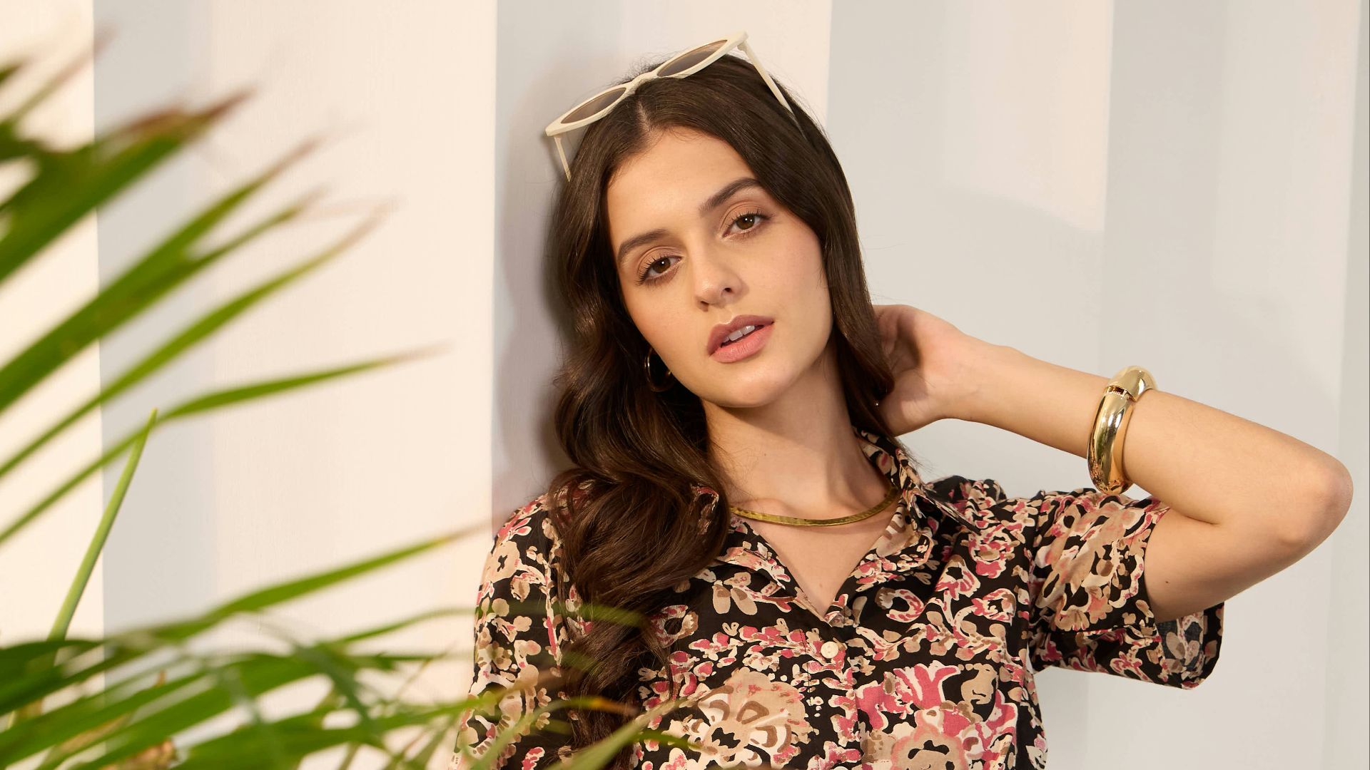 Woman in floral jumpsuit leans against wall