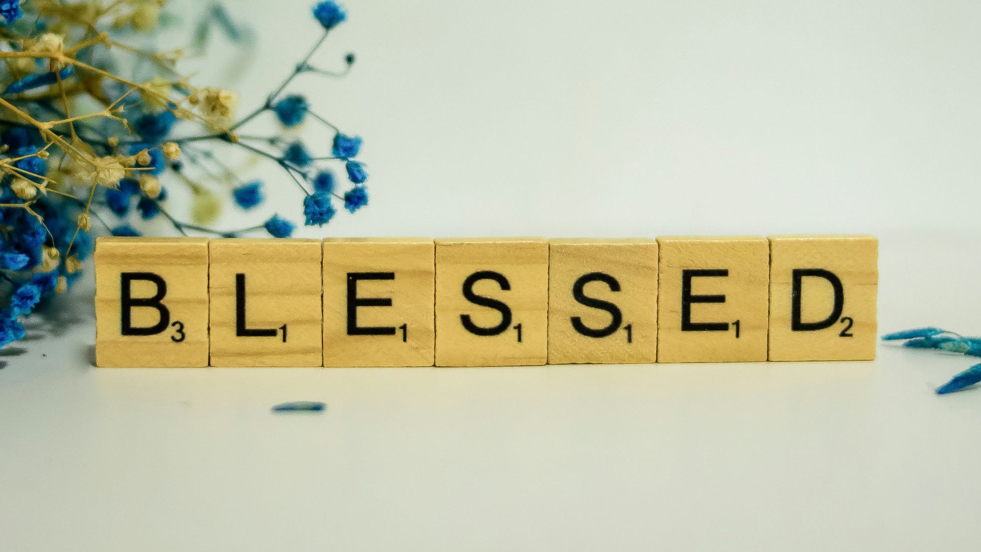 a wooden block spelling the word blessing next to a bouquet of blue flowers