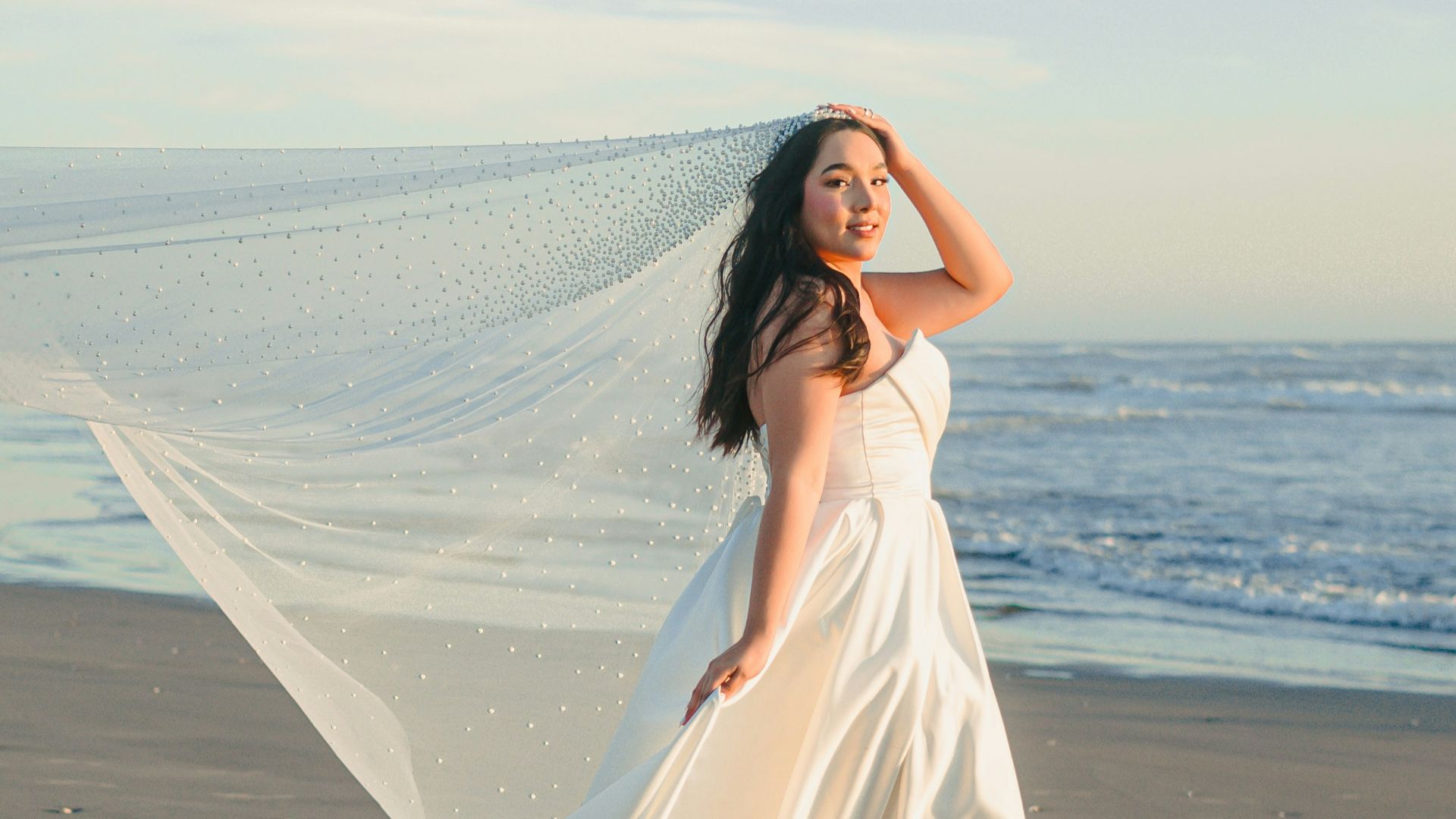 Bride in white dress on beach with veil blowing