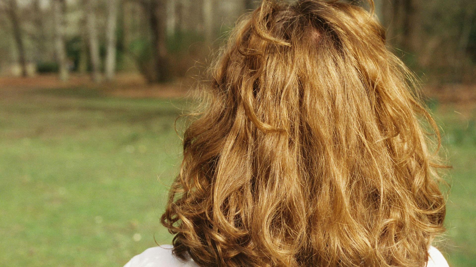 Woman with long curly blonde hair in a park.