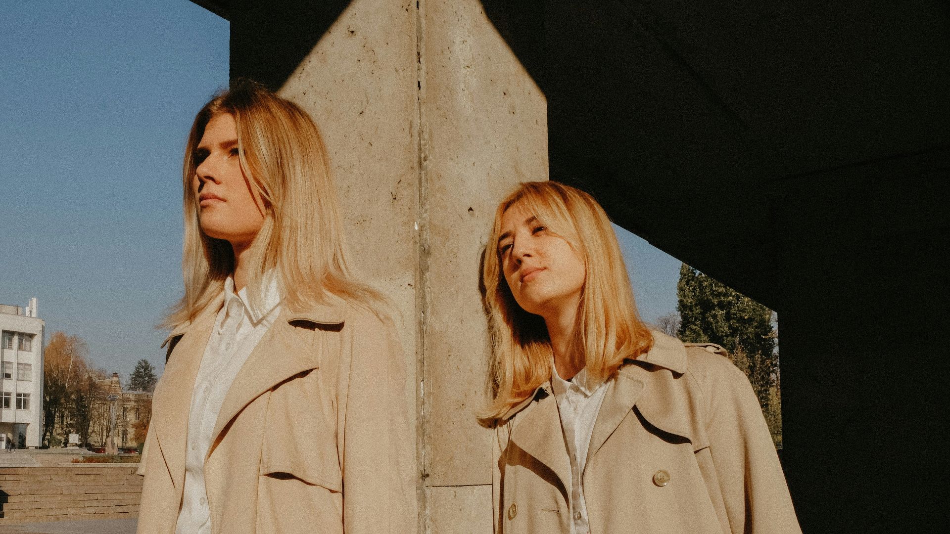 two women wearing brown coat leaning on concrete pillar
