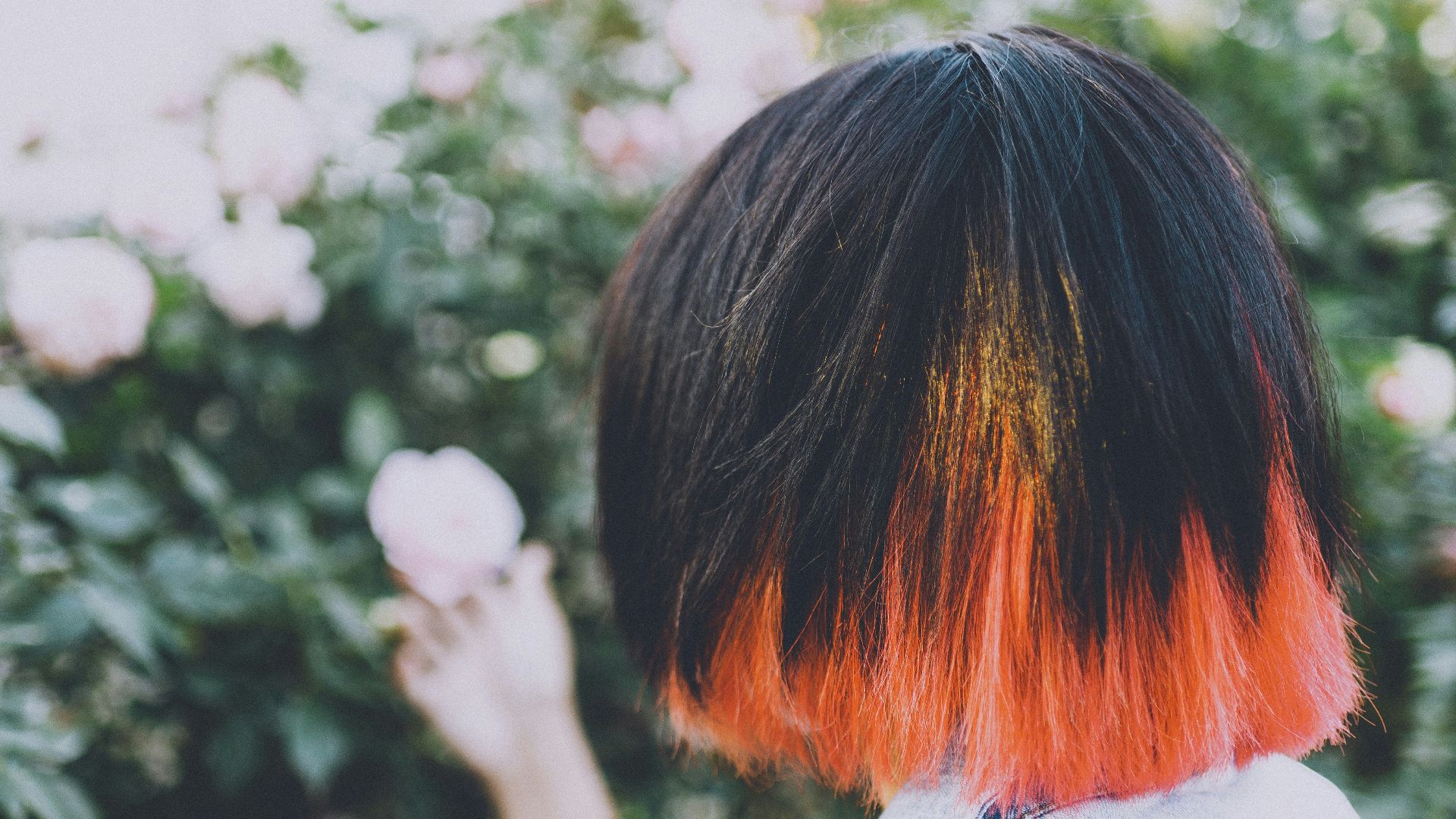 a woman with orange and black hair holding a flower
