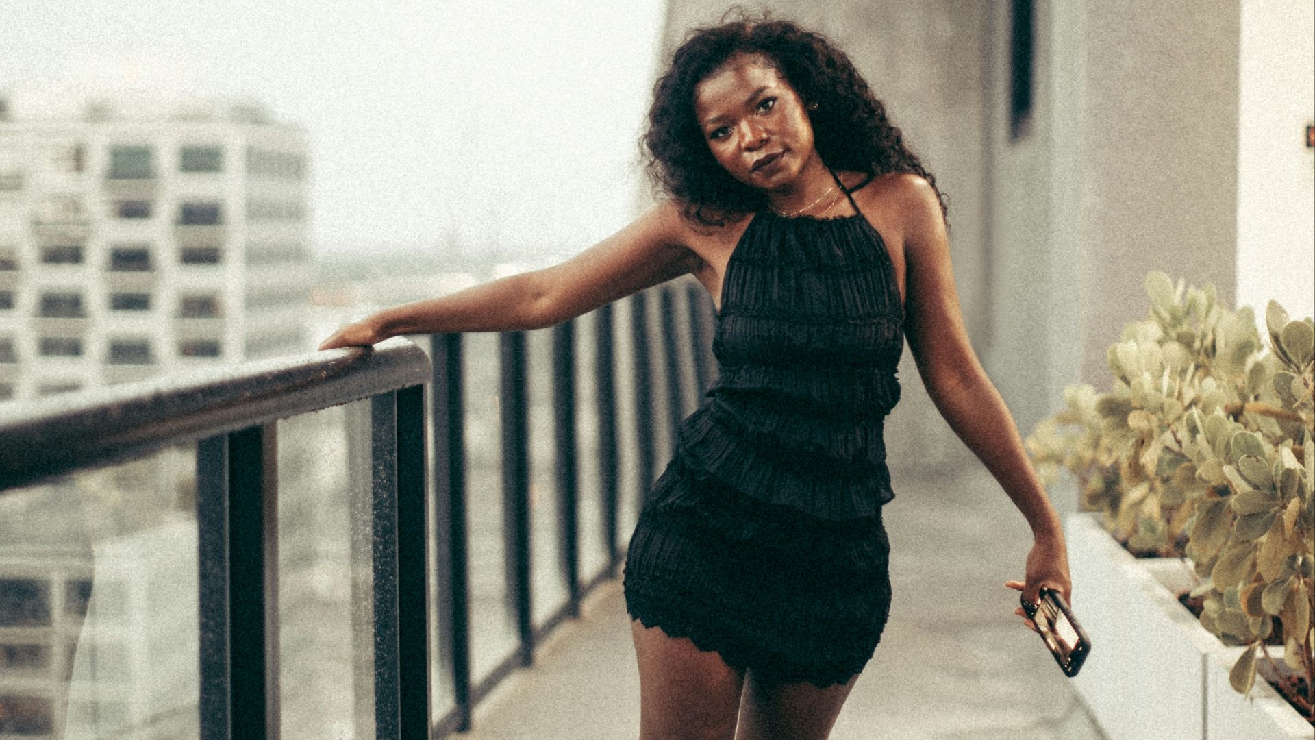 Woman poses on a balcony overlooking a cityscape.