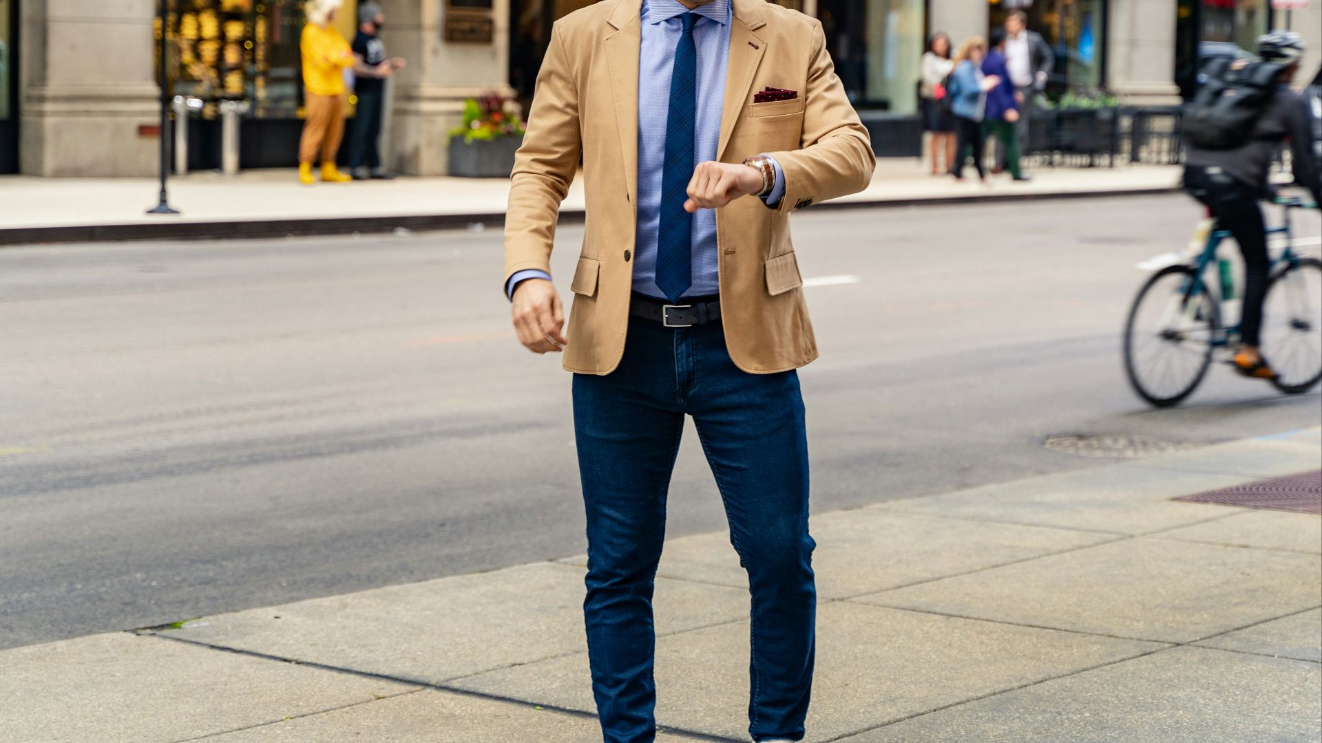 person in blue denim jeans and brown coat standing on sidewalk during daytime