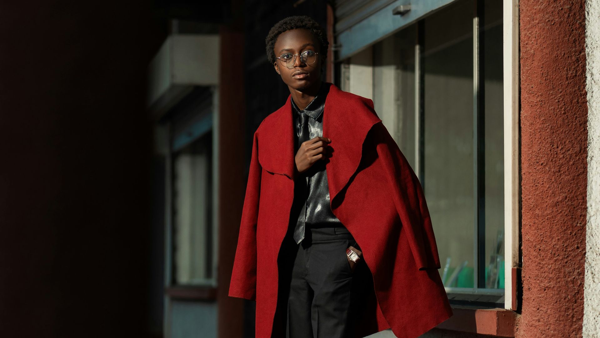Young man in red coat stands by window.