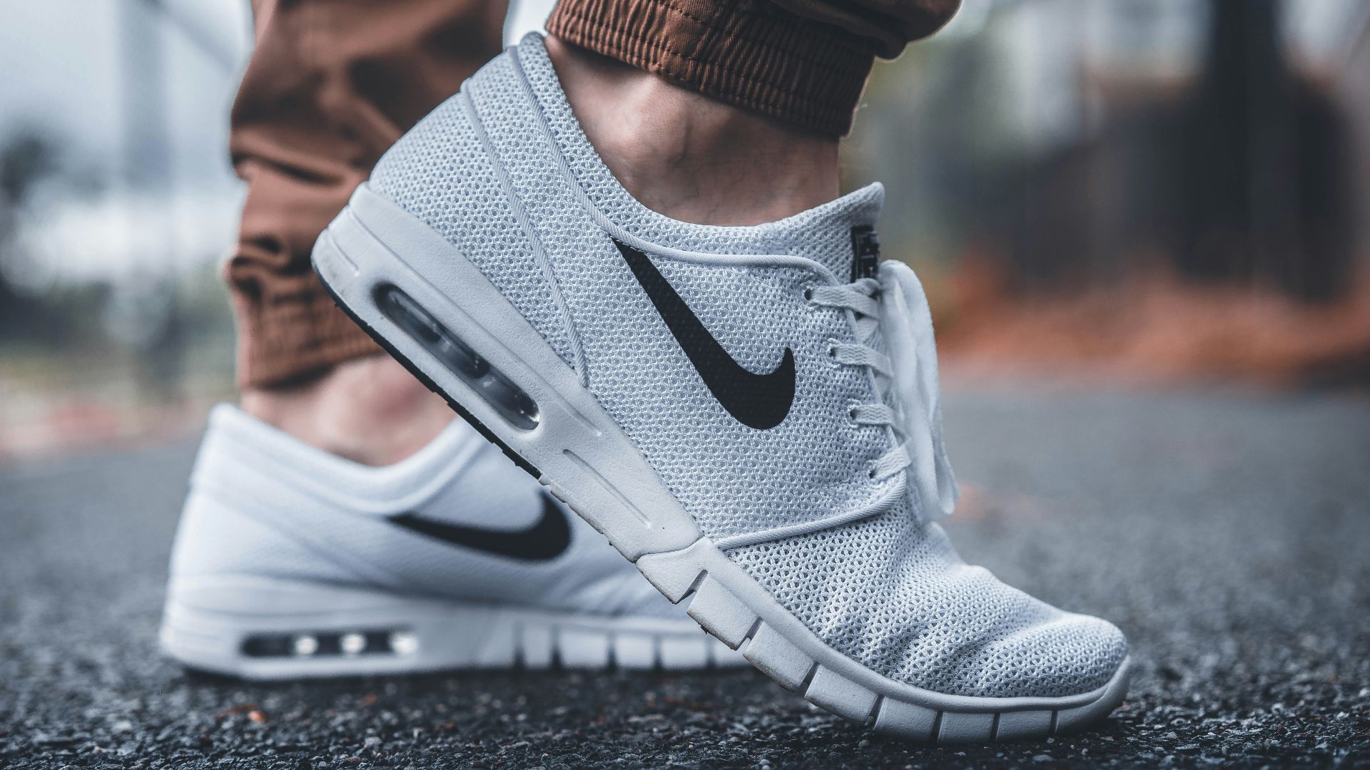 person wearing white Nike running shoes standing on black concrete path