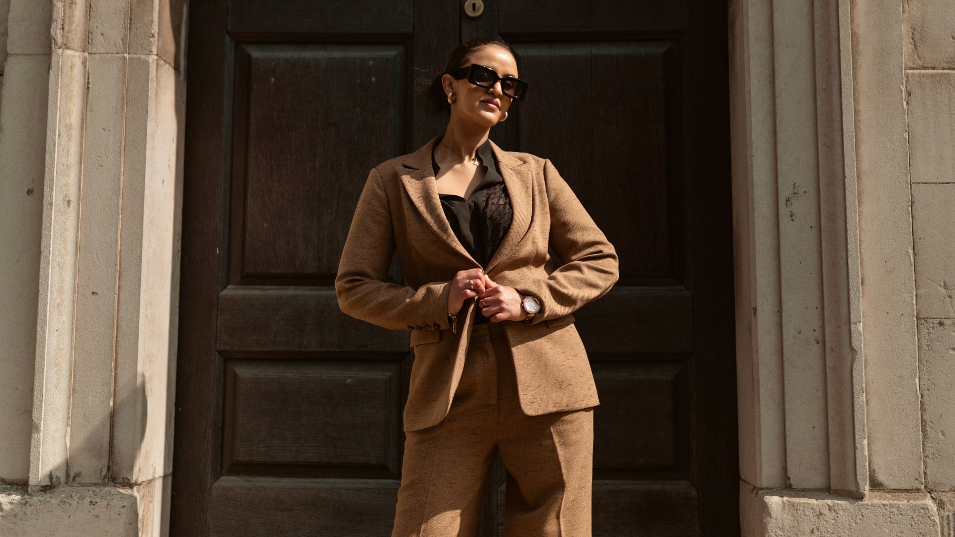 A stylish woman in a brown pantsuit poses.